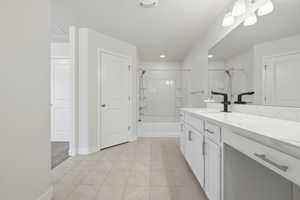 Bathroom featuring a double vanity with white cabinetry and a light-toned countertop, matte black faucets, a large wall-mounted mirror, and tile flooring