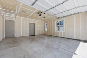 Spacious two-car garage featuring a concrete floor, two windows, two entry doors, and overhead storage shelving