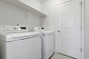 Dedicated utility space featuring a white top-load washer, a white dryer, and a white wall-mounted storage shelf