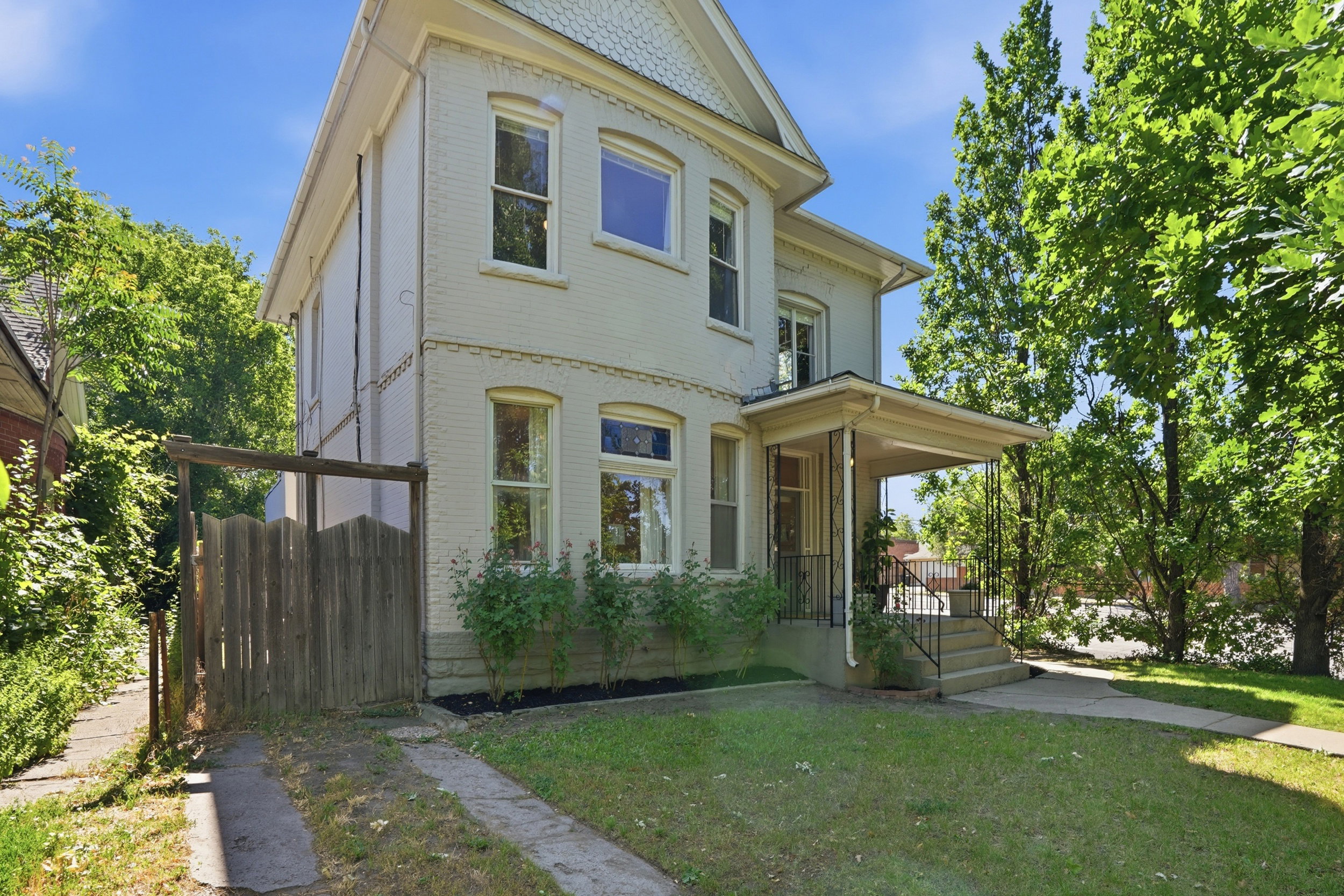 Two-story property featuring a covered front porch, a well-maintained lawn, and mature trees