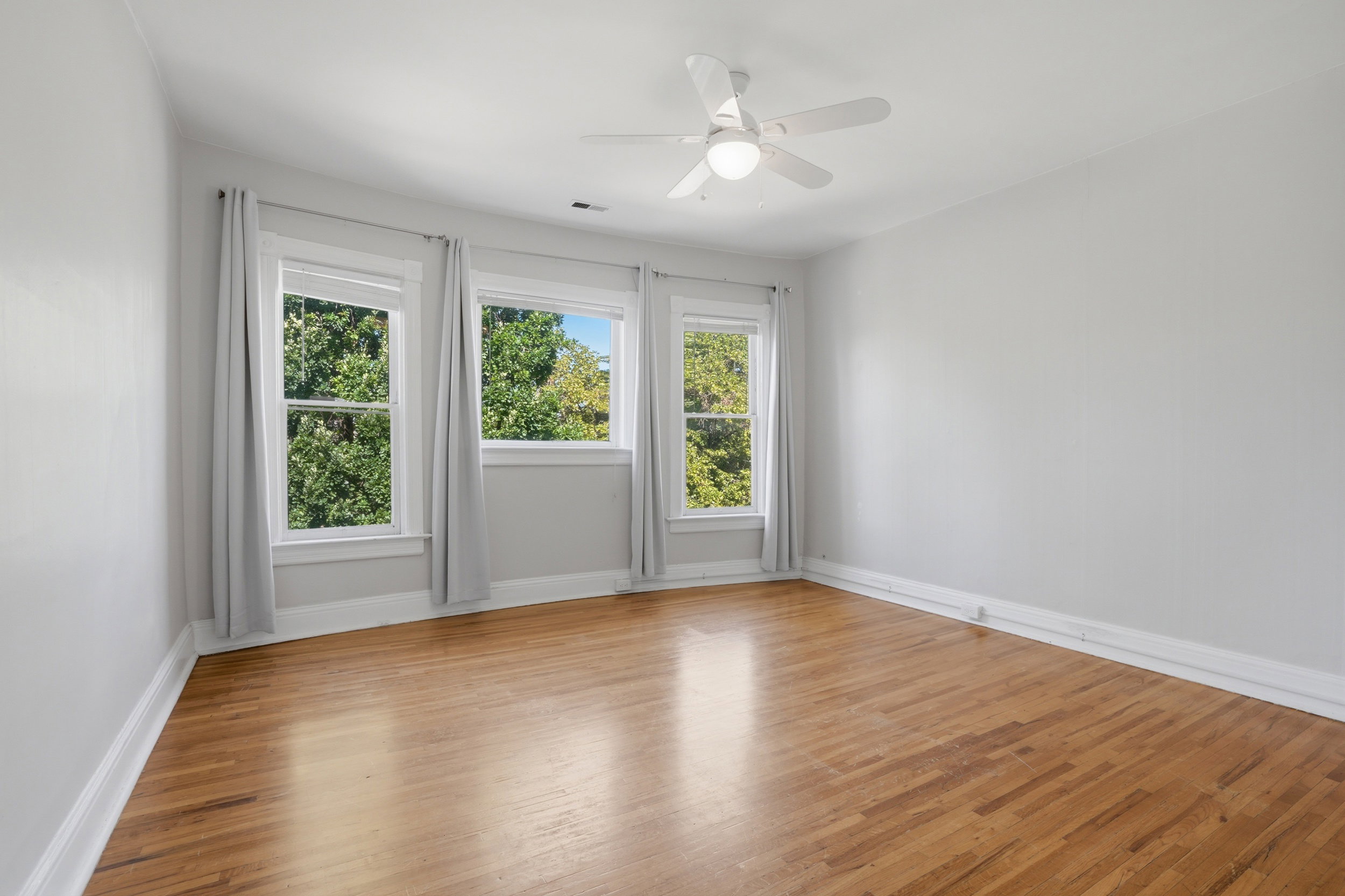 Room featuring five large windows, wood-finish flooring, a white ceiling fan with integrated lighting, and light-colored walls