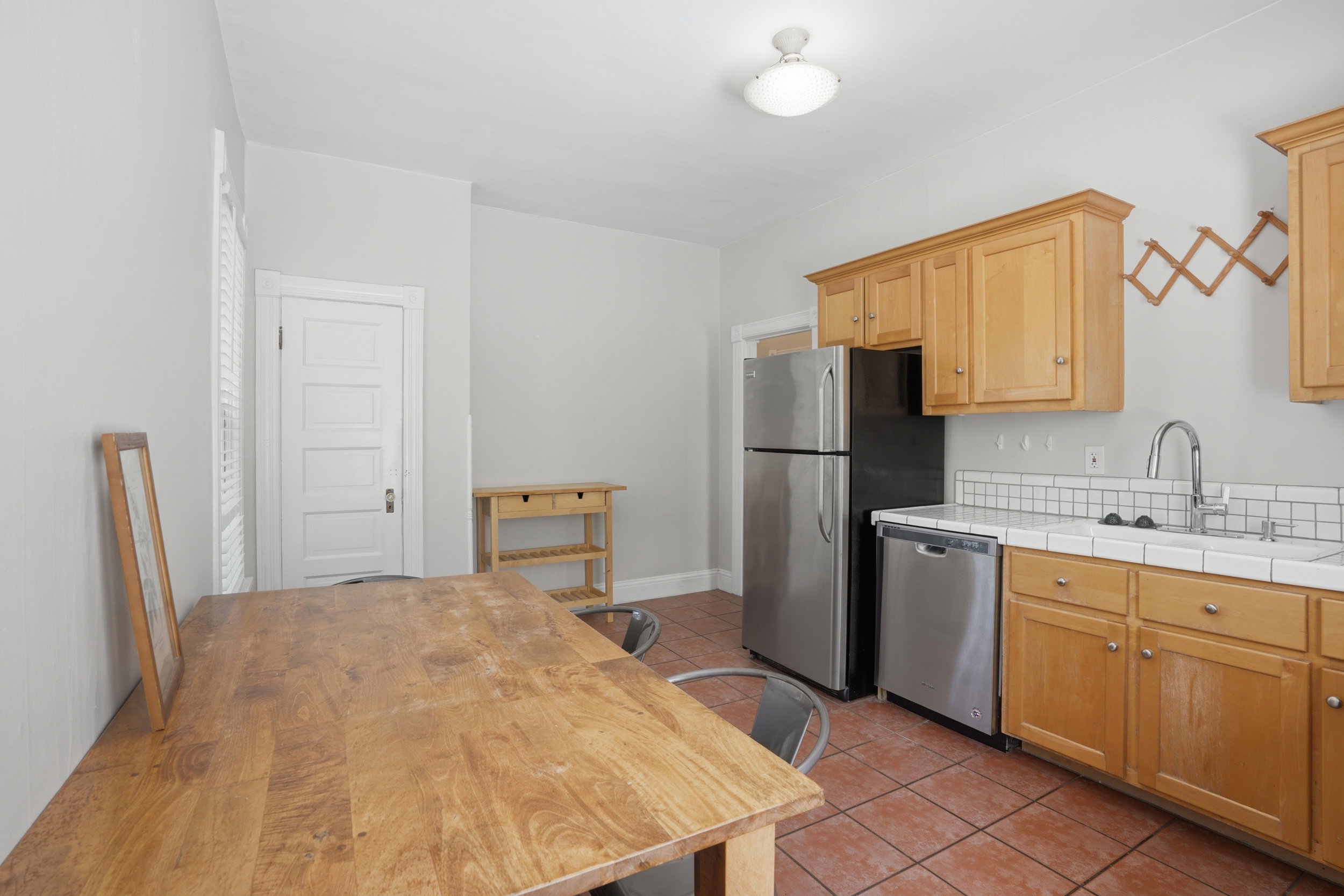 Kitchen featuring light wood cabinetry, white tile countertops, subway tile backsplash, stainless steel appliances, and terracotta tile flooring