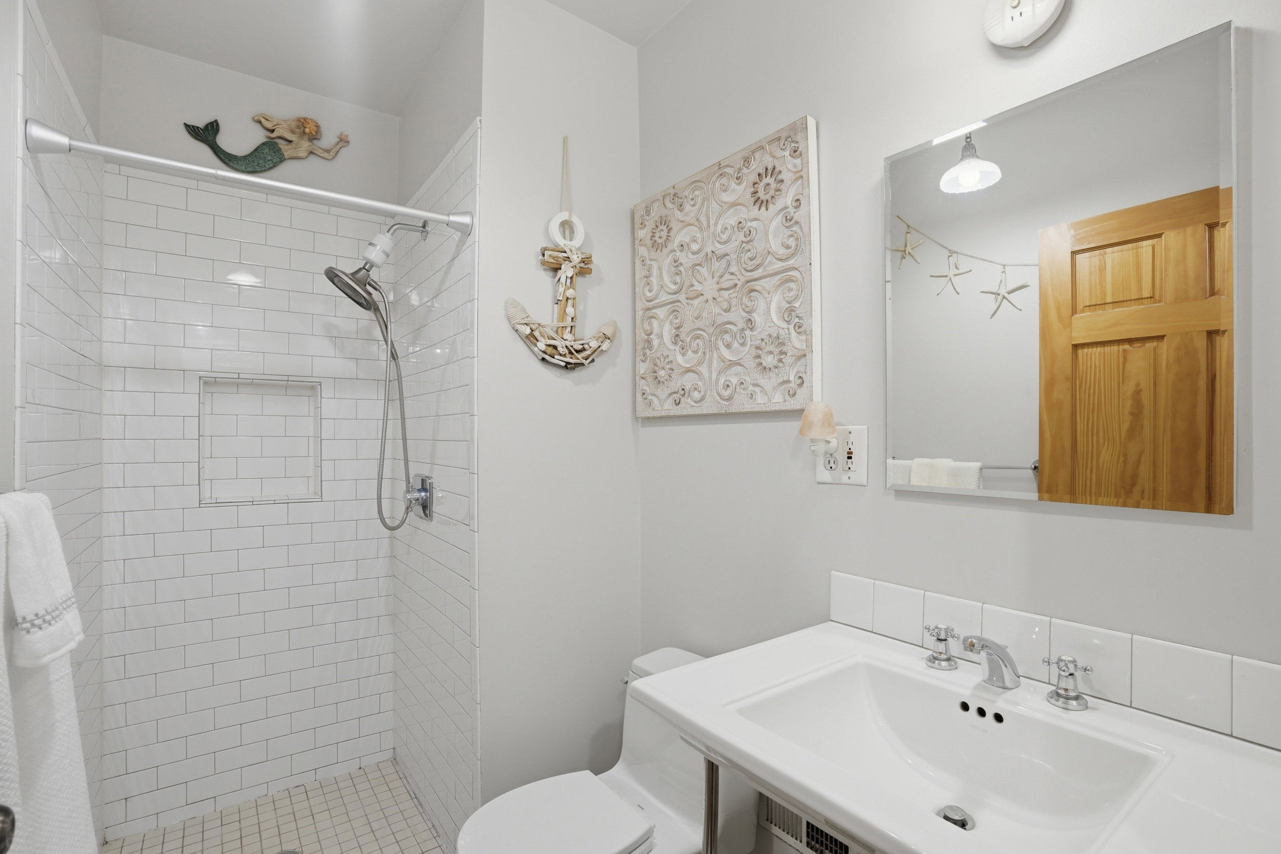 Bathroom featuring a white subway tile shower with a recessed niche, a shower head with an adjustable hose, a white ceramic sink with a chrome faucet, a white vanity with a tile backsplash, and a frameless mirror