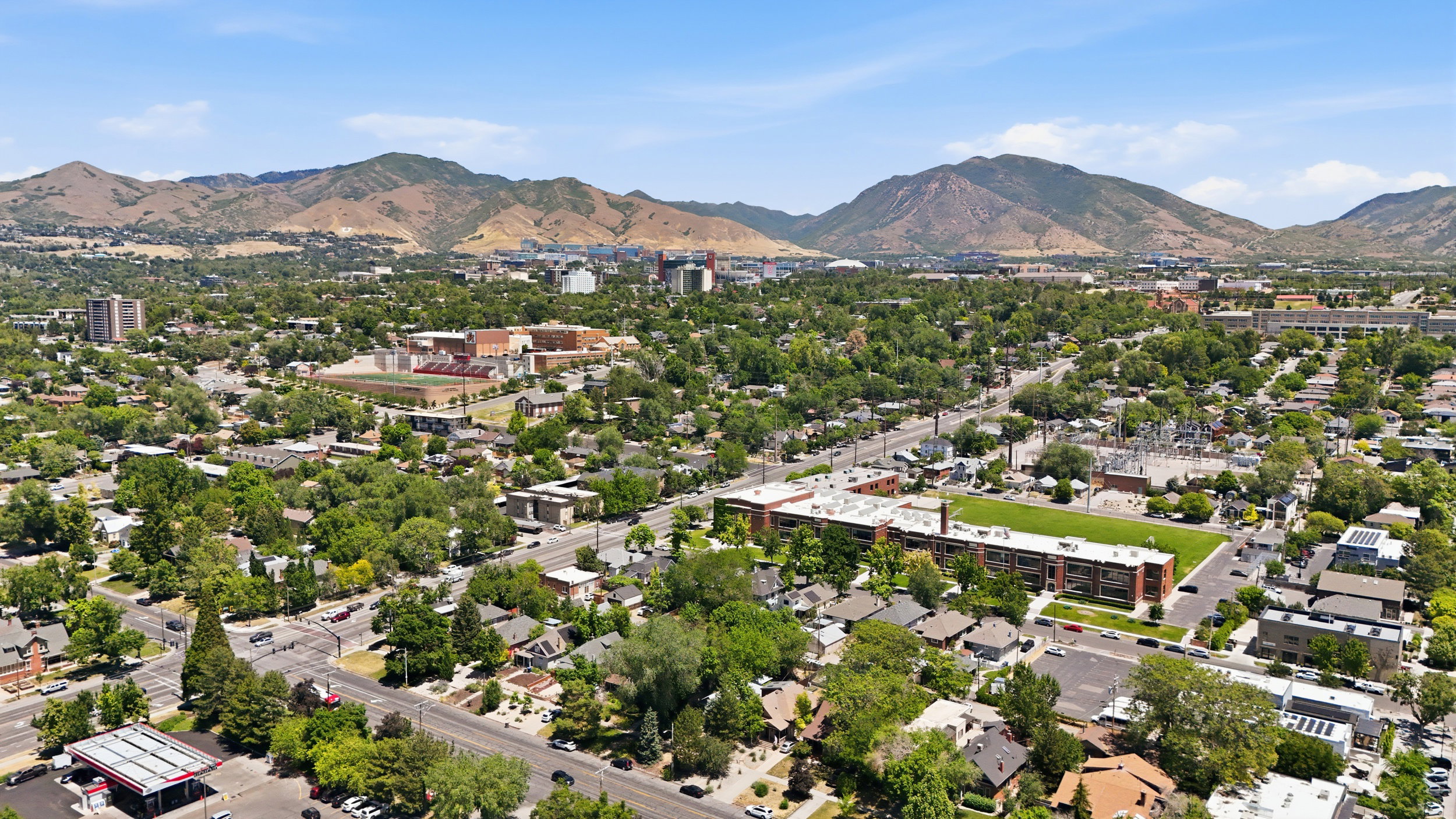 Expansive urban landscape featuring a mix of residential and commercial structures, mature green trees, and paved roadways