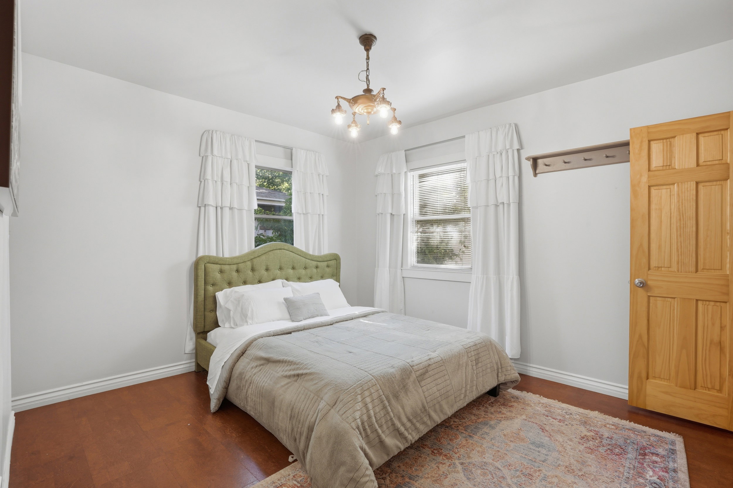 Bedroom featuring two window openings with white trim, wood-finish flooring, and a natural wood paneled door
