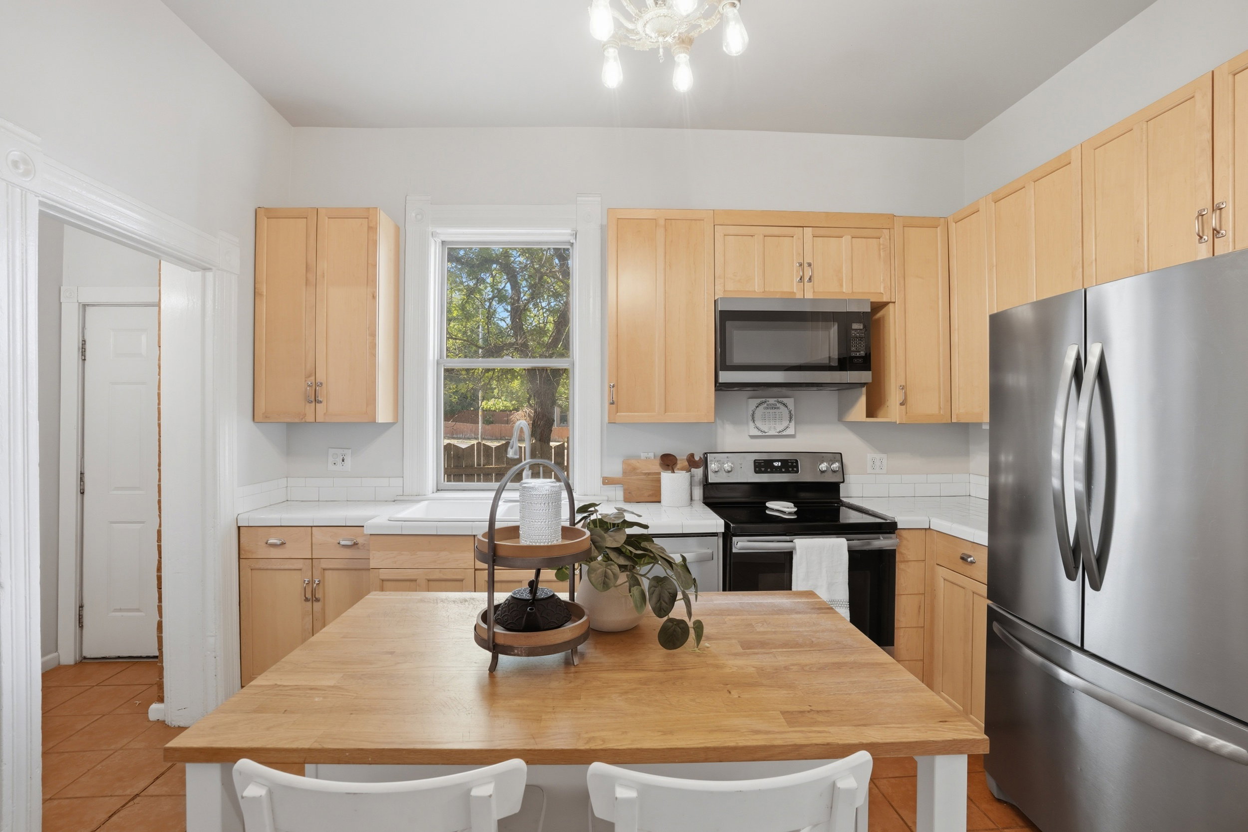 Kitchen featuring a central island with a wood-finish countertop, light wood cabinetry, white countertops, white subway tile backsplash, and stainless steel appliances