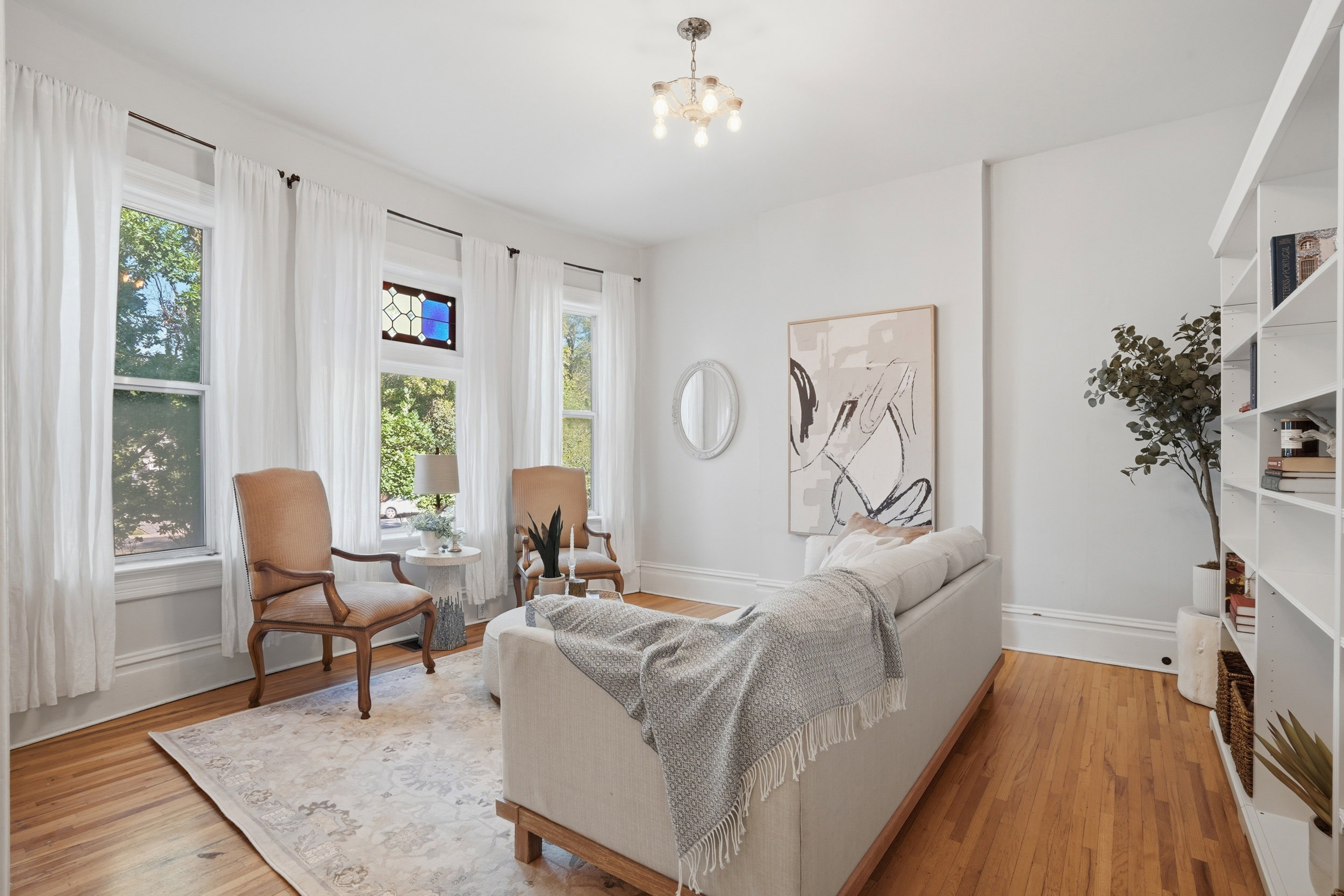 Hardwood flooring features throughout this living space, complemented by multiple sash windows and a stained glass transom window