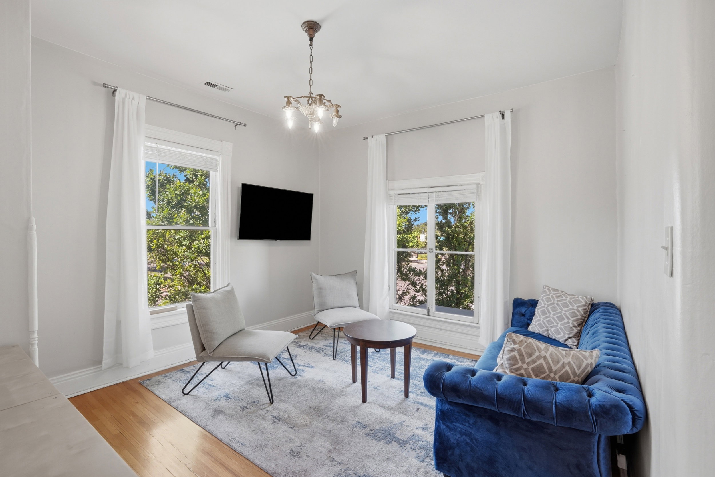 Bright living space featuring natural light, wood-finish flooring, high ceilings, a decorative chandelier, and white window treatments