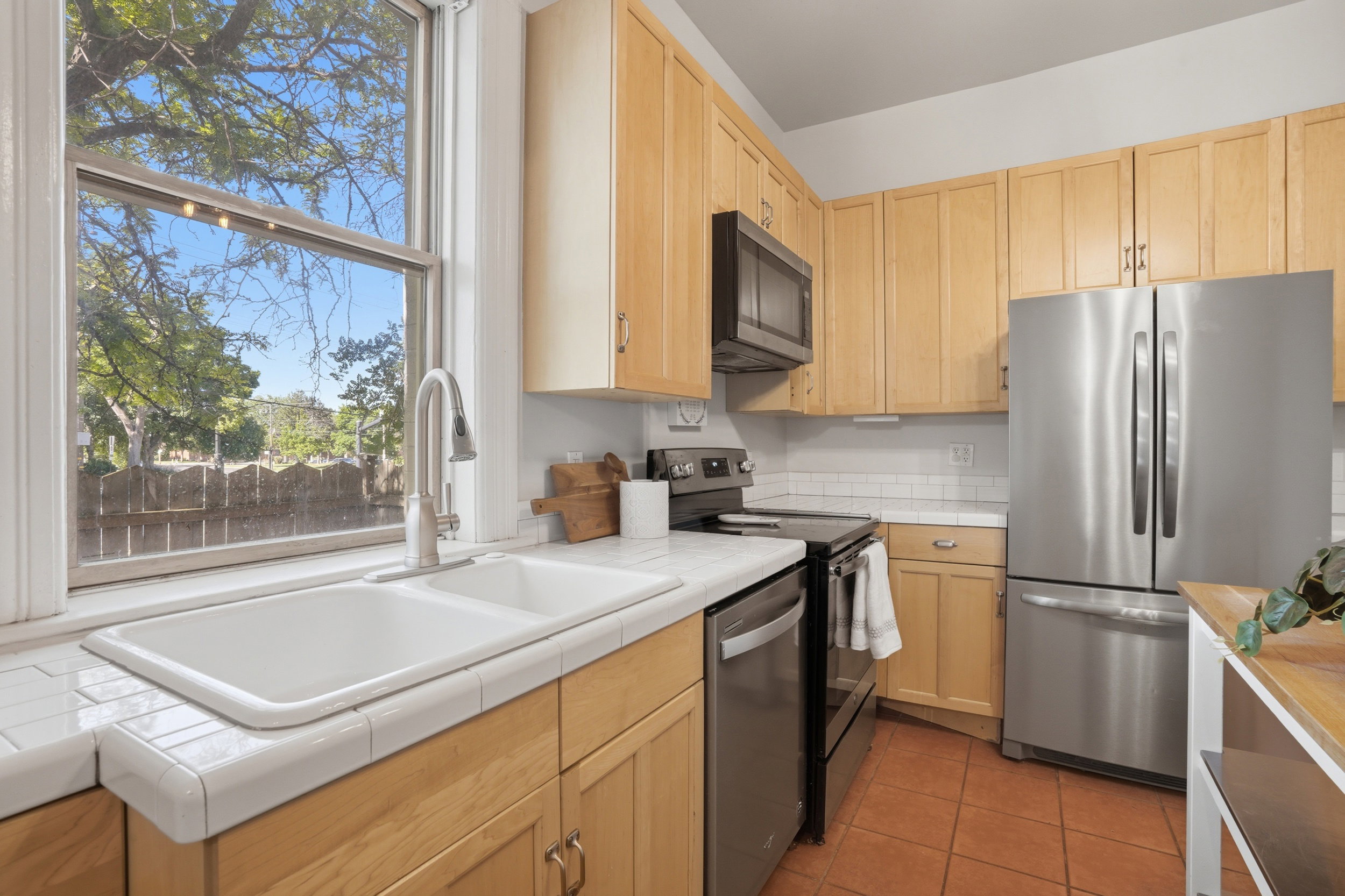 Kitchen featuring light wood cabinetry, a double basin sink, white tiled countertops, and a white subway tile backsplash
