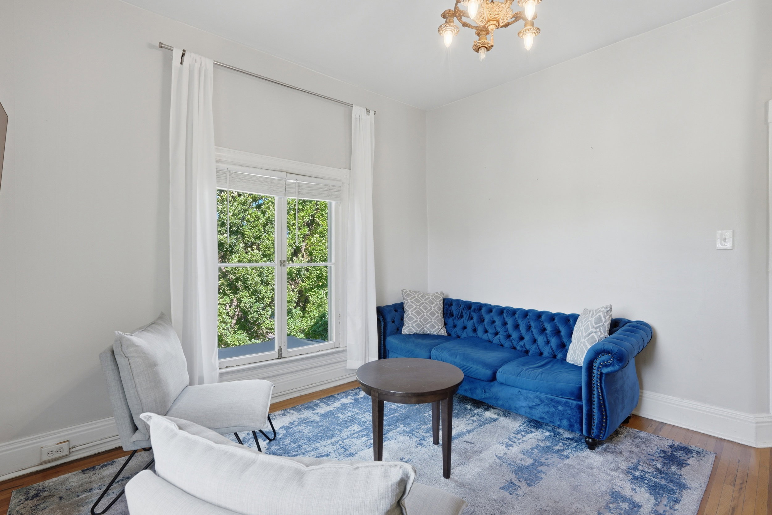 Hardwood flooring complemented by white baseboards, a large double window with white trim, and an ornate ceiling fixture