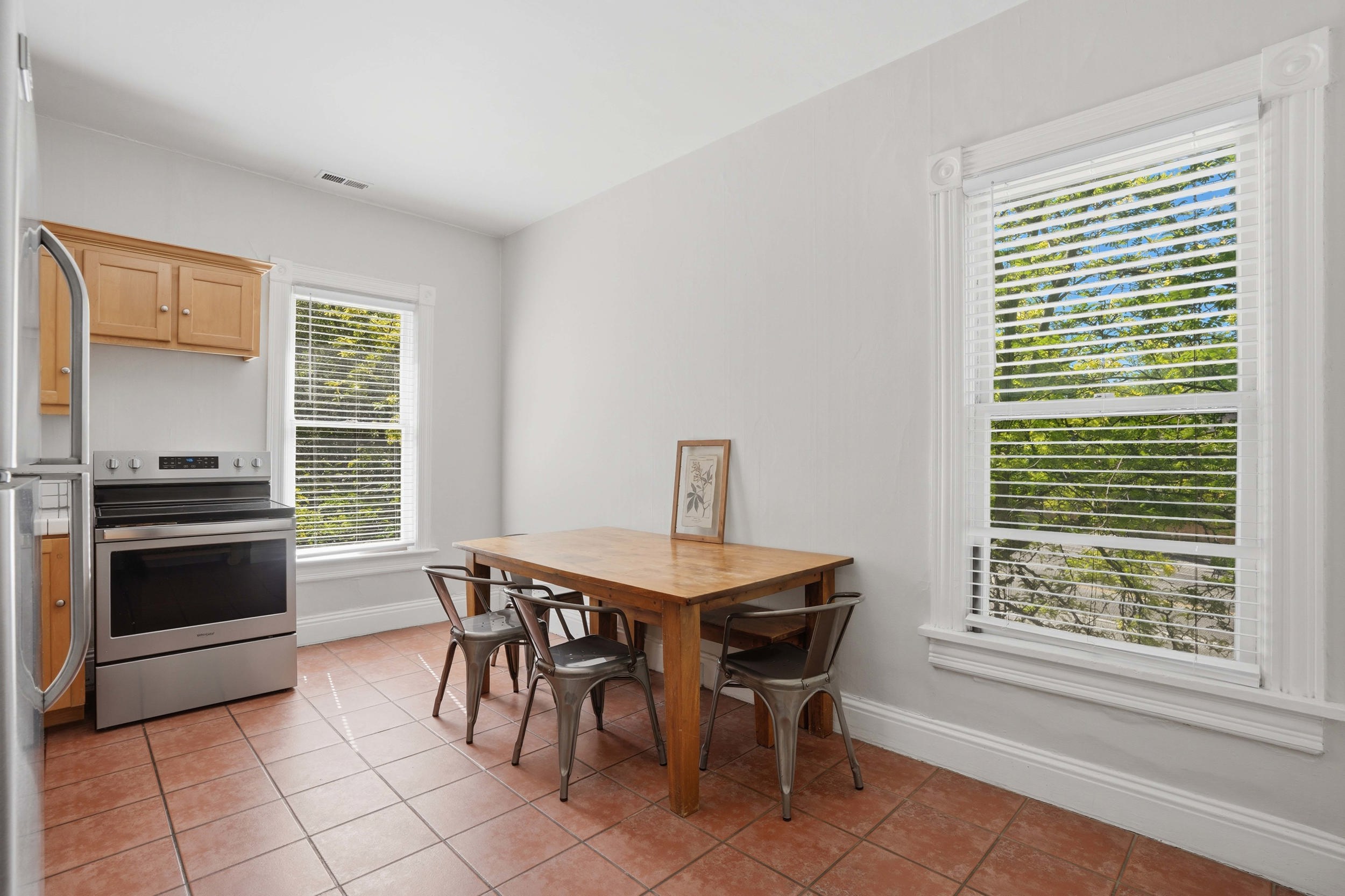 Dining area featuring terracotta-style floor tiles, two large windows with ornate trim, and light-toned wall paint