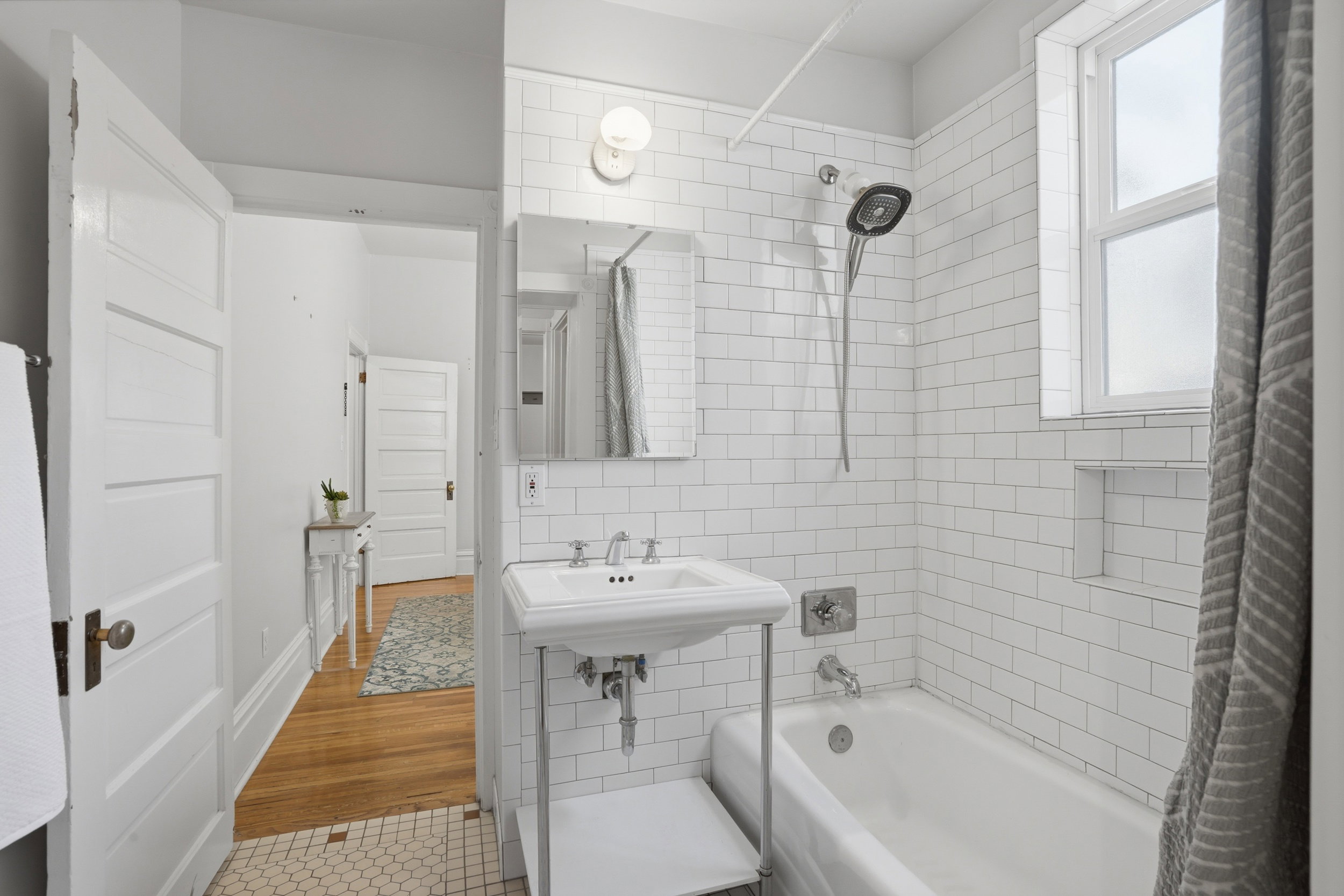 Bathroom featuring white subway tile surround, a pedestal sink with chrome fixtures, and a classic white bathtub