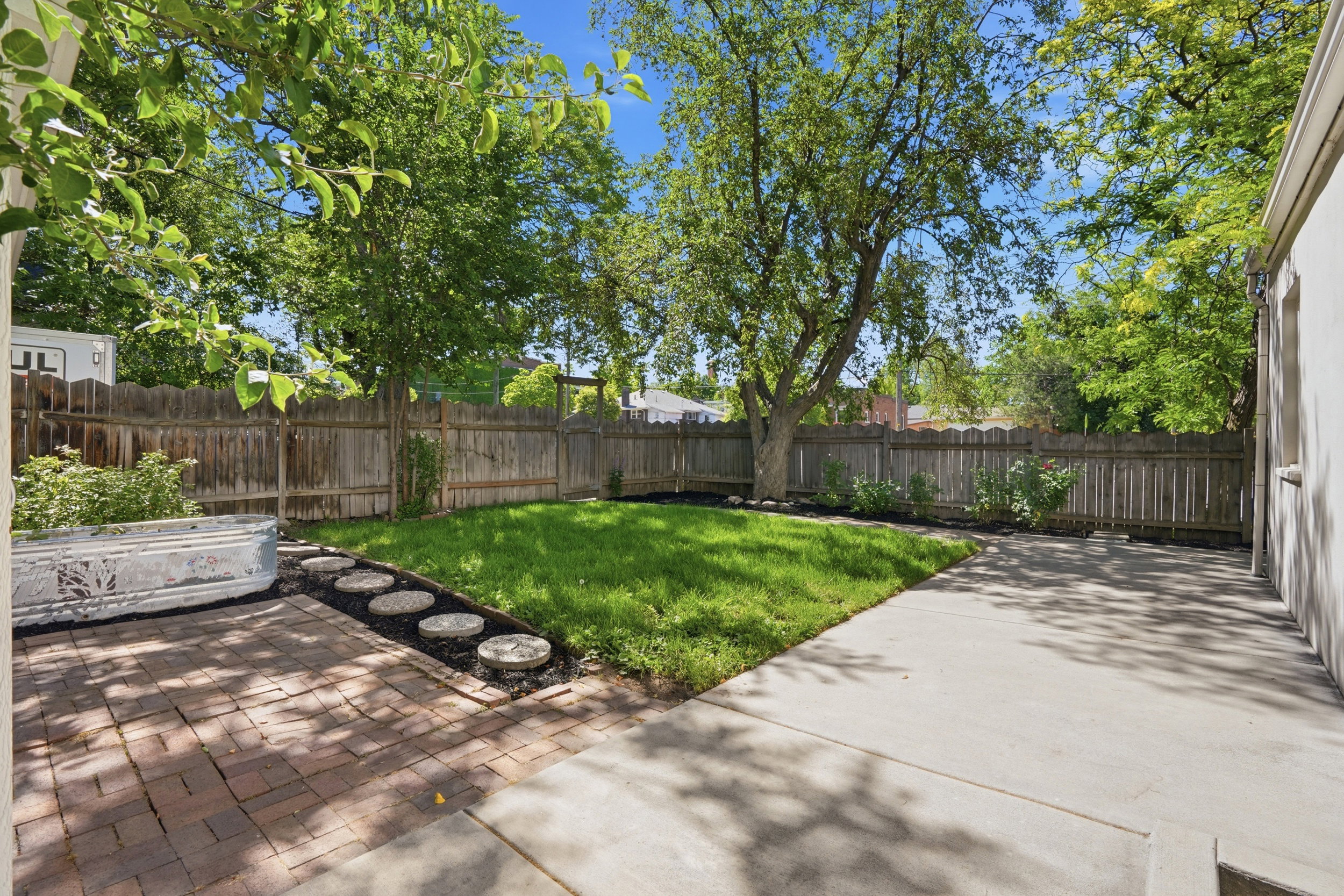 Private backyard featuring a concrete patio, a brick-paved patio, a manicured lawn, mature trees, and a wood privacy fence