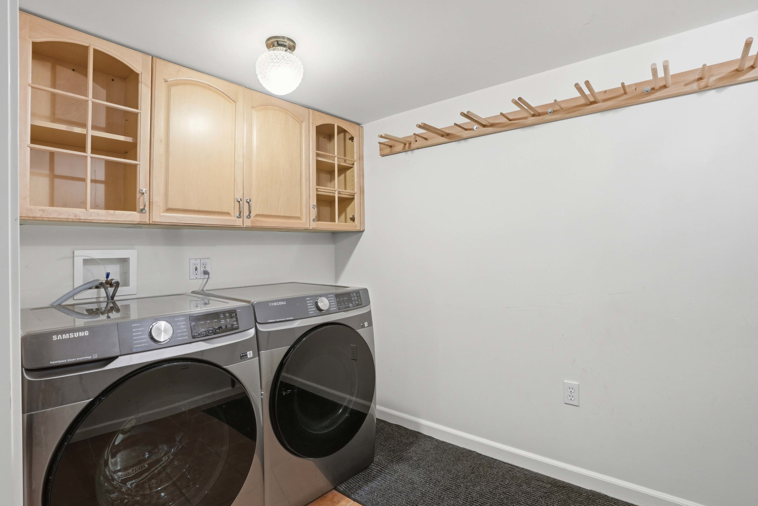 Laundry area featuring light wood cabinetry, a decorative ceiling light fixture, and a wooden drying rack