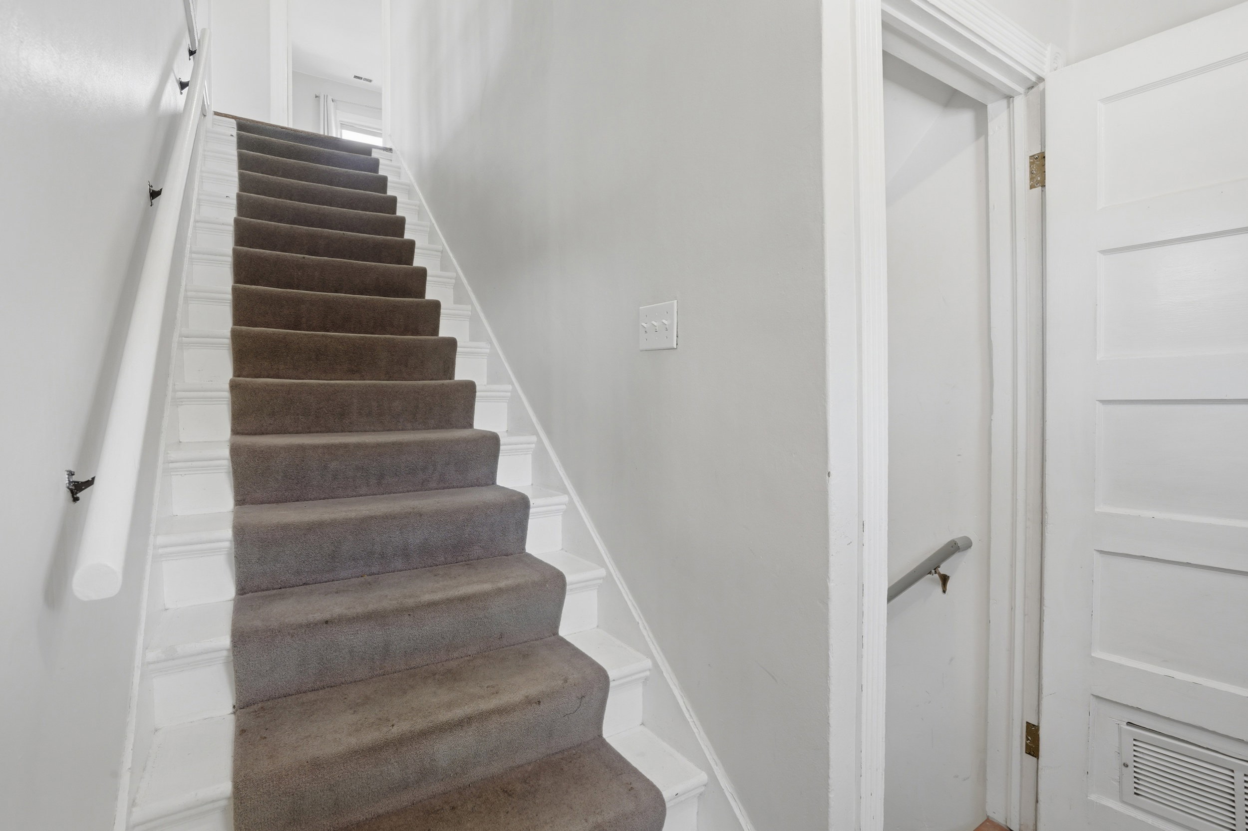 Carpeted staircase with white risers and a white handrail