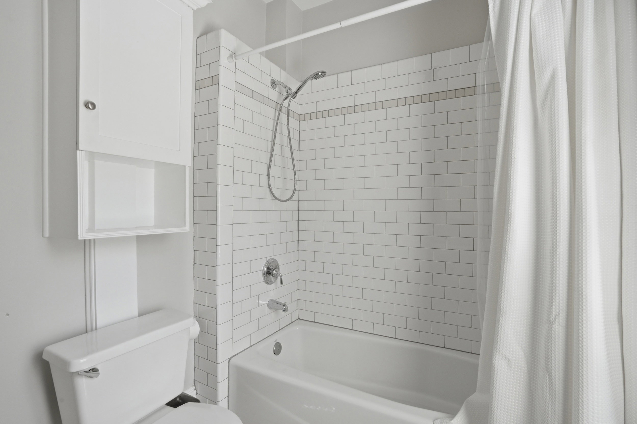 Bathtub and shower combination featuring subway tile surround with decorative accent band