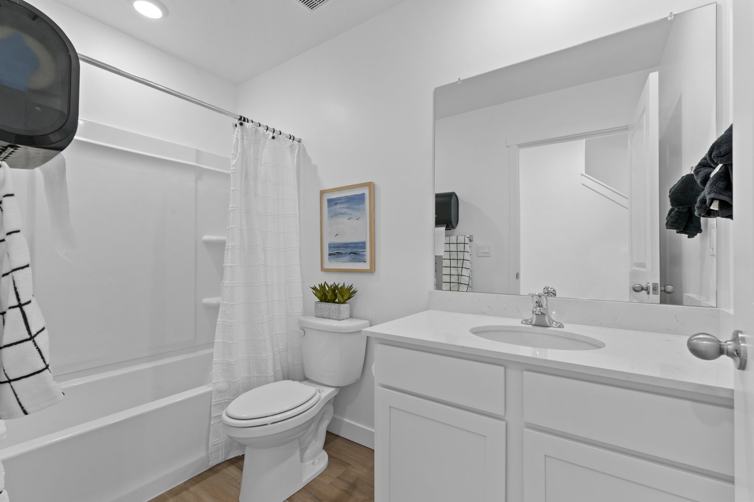 Bathroom featuring a white vanity with an undermount sink, a large wall-mounted mirror, a tub/shower combination, wood-finish flooring, and a white toilet