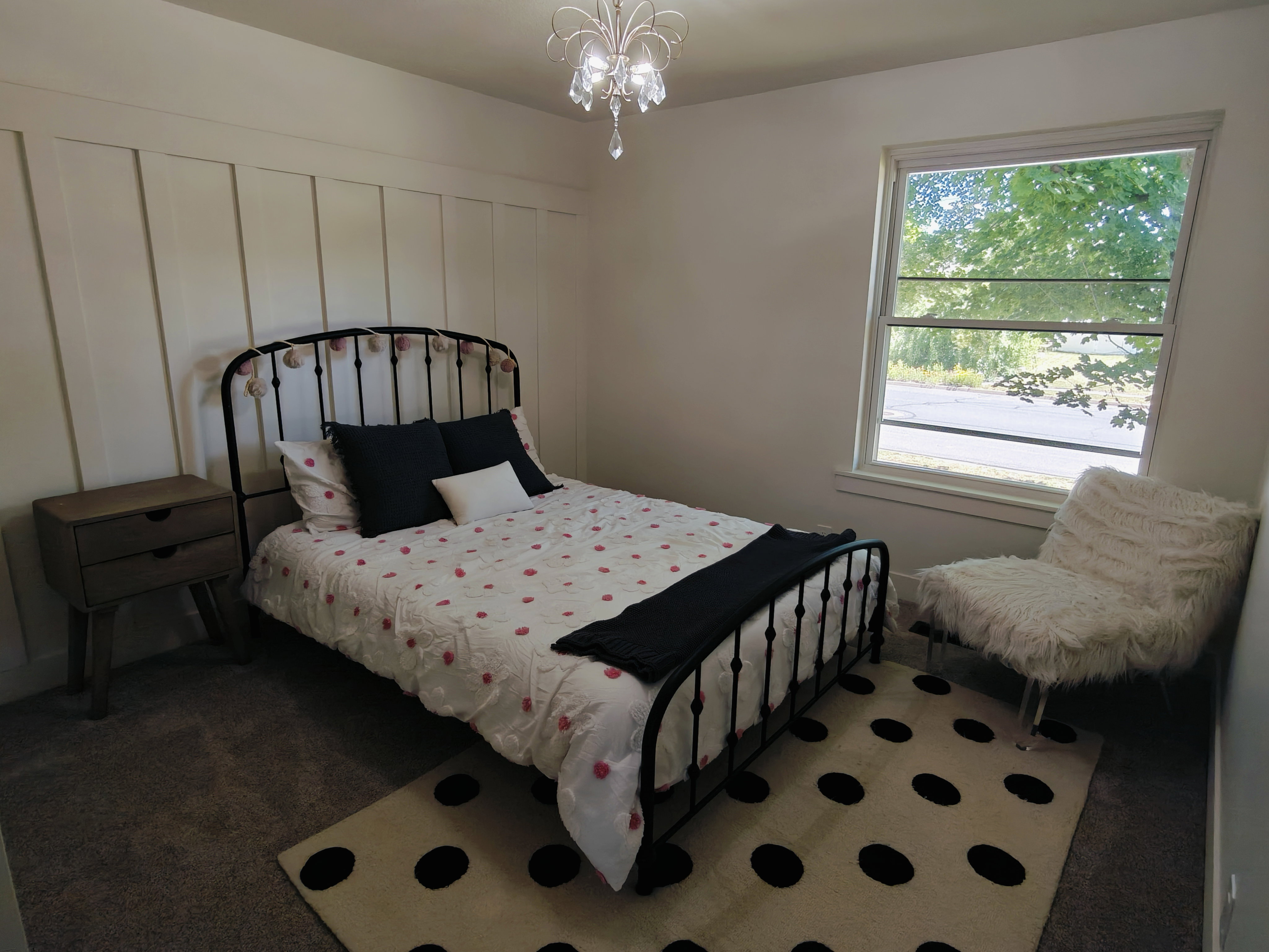Bedroom featuring wainscoting accent wall, a chandelier light fixture, double-hung window, and carpet flooring