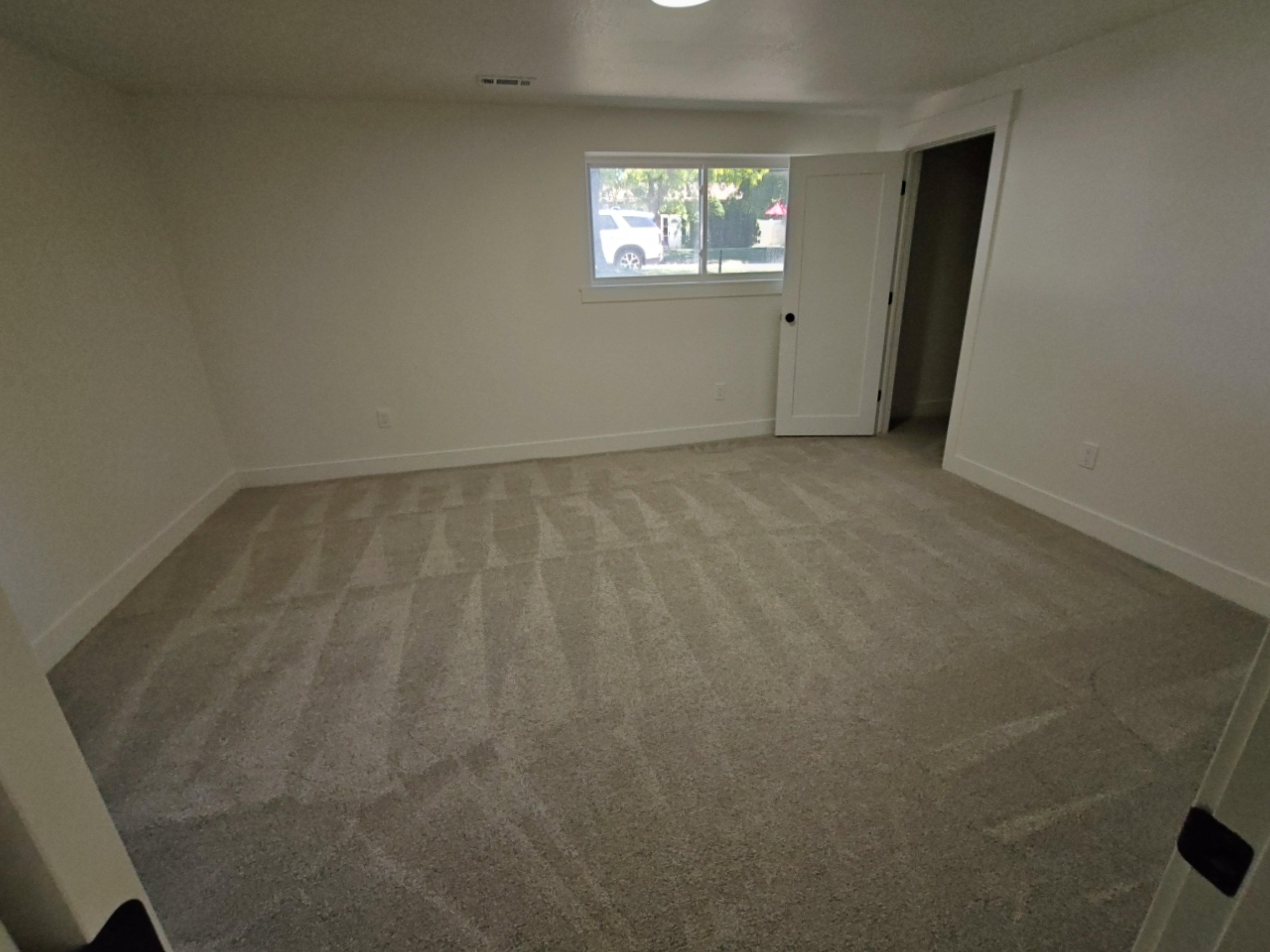 Spacious room featuring new carpeting, white baseboards, and a window with natural light
