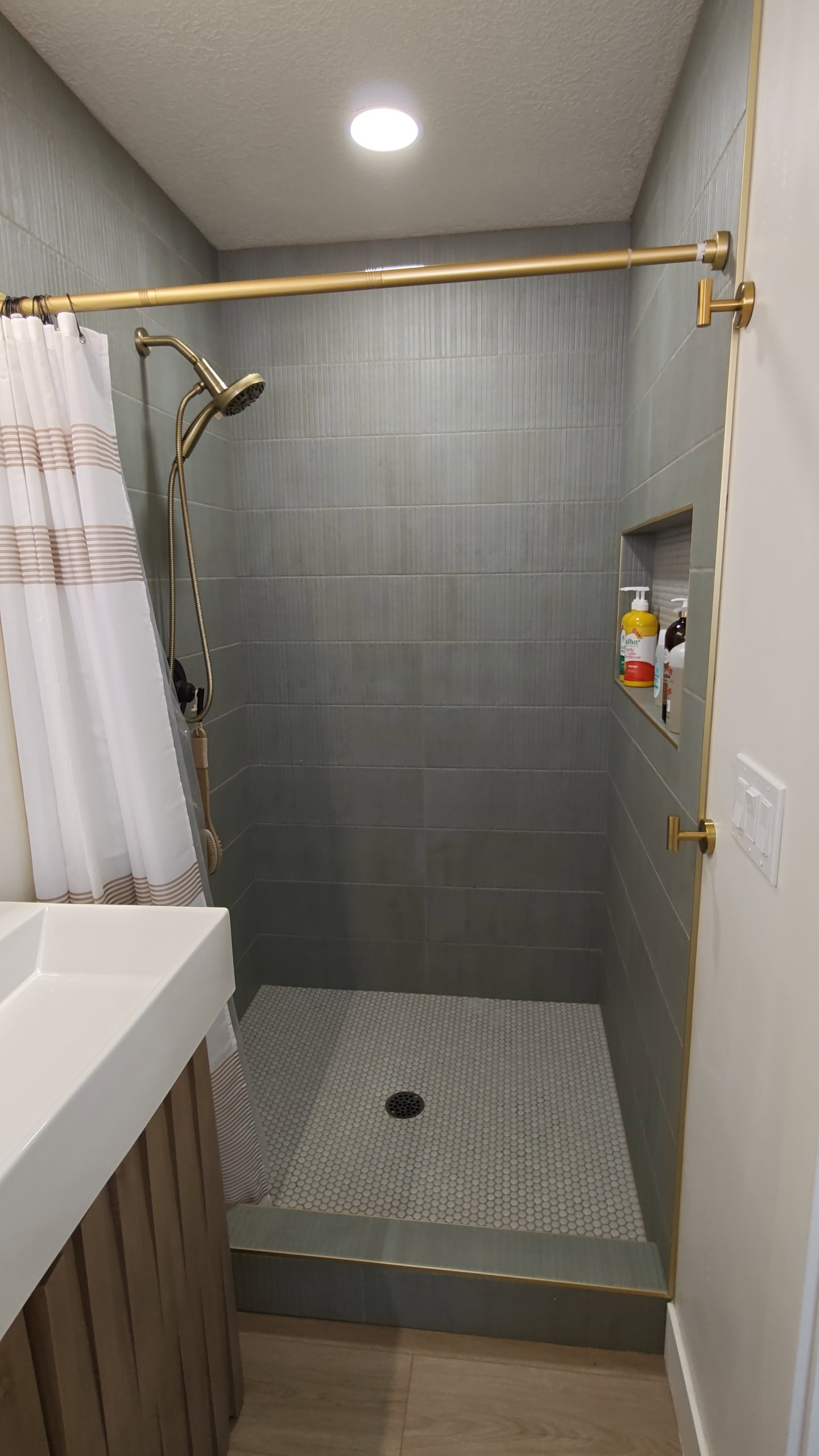 Shower enclosure featuring horizontal gray tile walls and a mosaic tile floor