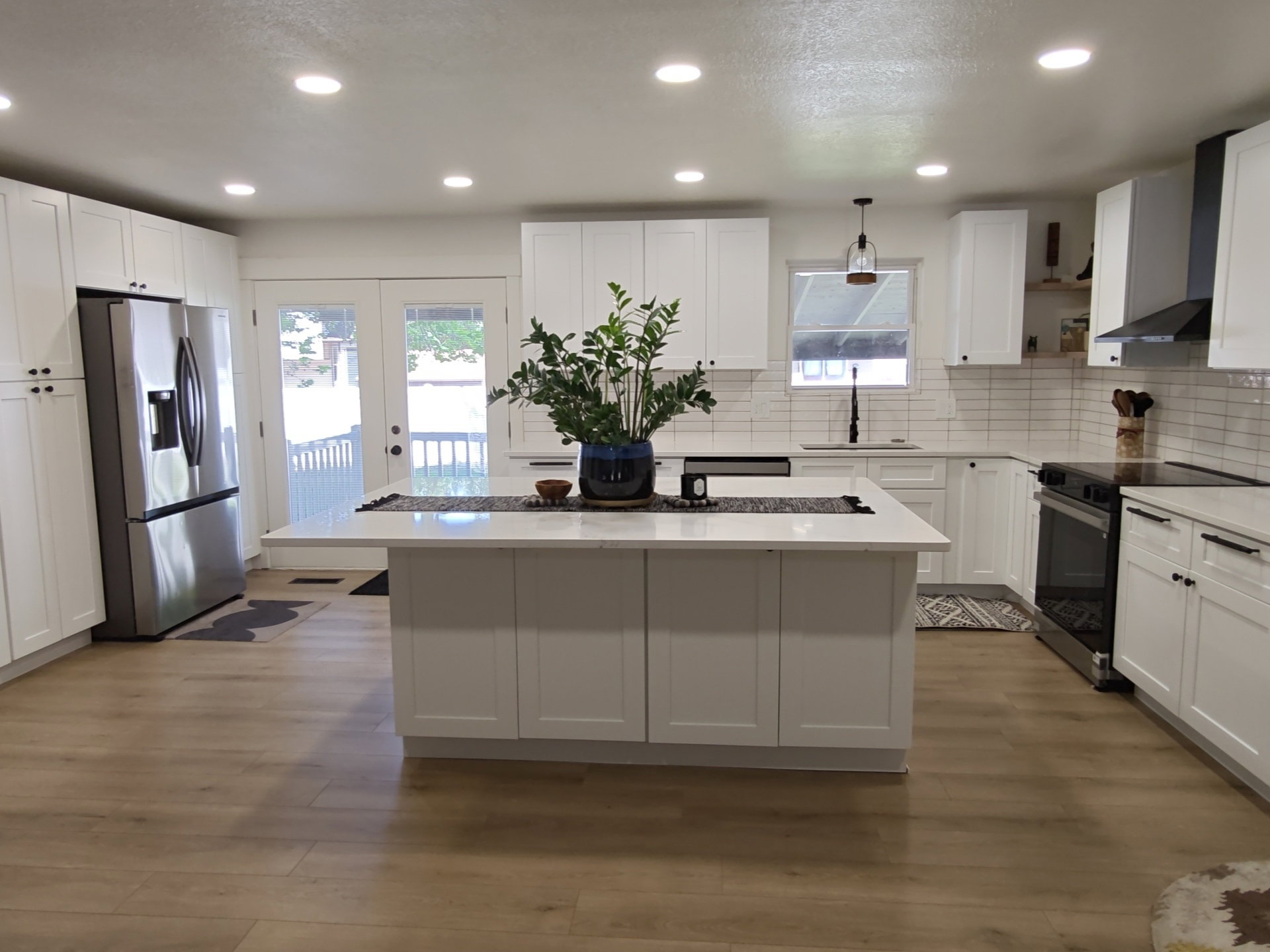 Well-appointed kitchen featuring light wood-finish flooring, white shaker cabinetry, and a subway tile backsplash