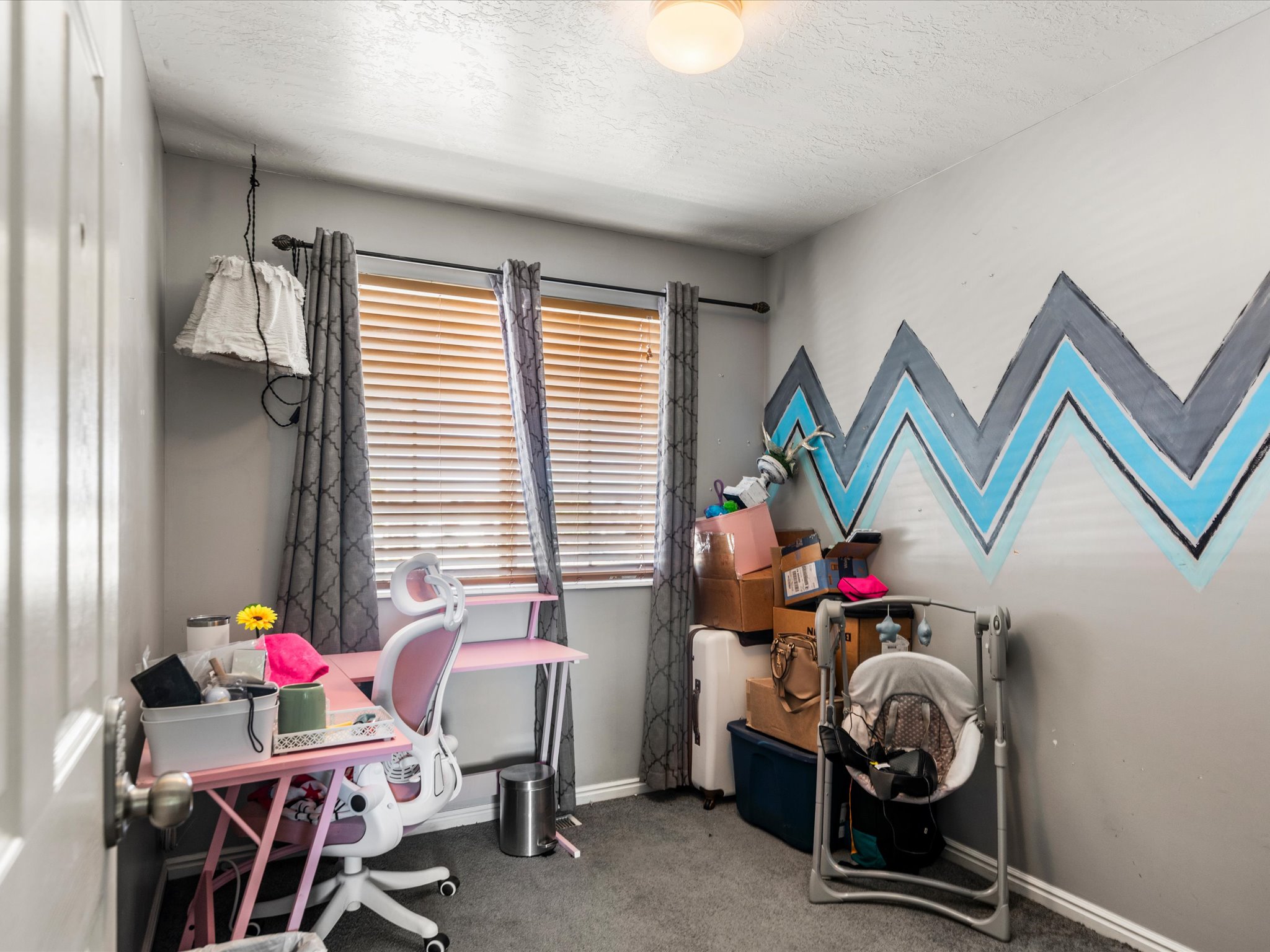 Carpeted interior room with a window featuring horizontal blinds