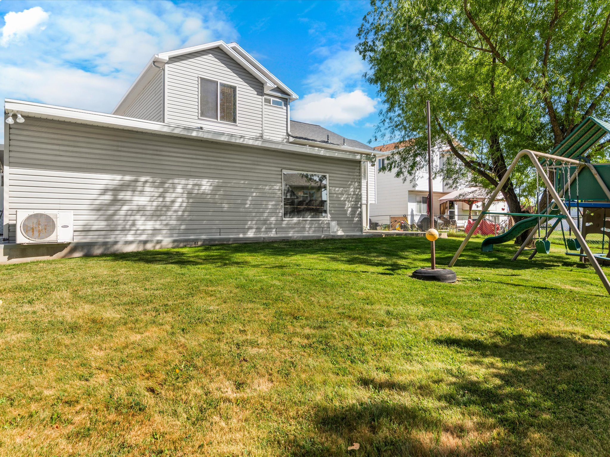 Expansive lawn area featuring a mature tree, a full swing set, and a residential structure with horizontal siding and multiple windows