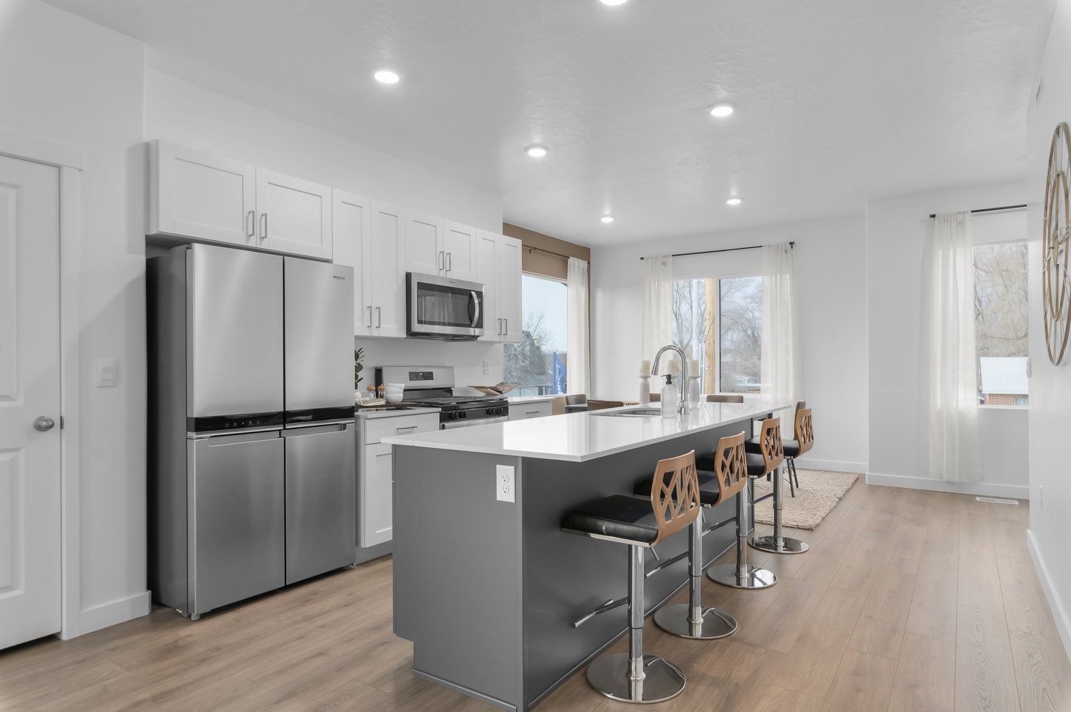 Contemporary kitchen featuring a large center island with seating, stainless steel appliances, light wood-finish flooring, white cabinetry, and recessed lighting
