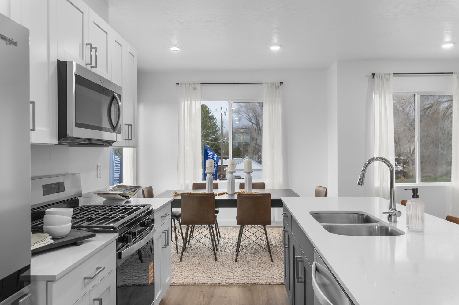 Contemporary kitchen featuring white cabinetry, stainless steel appliances, a gas range, white countertops, and an island with a double basin sink