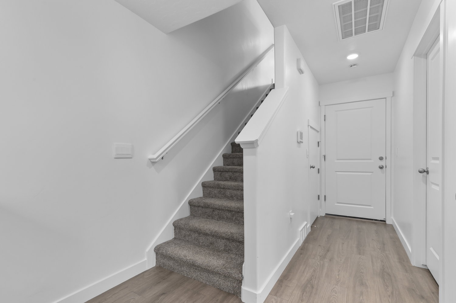 Entryway featuring wood-finish flooring, white walls, a carpeted staircase with white railing, and a solid white door