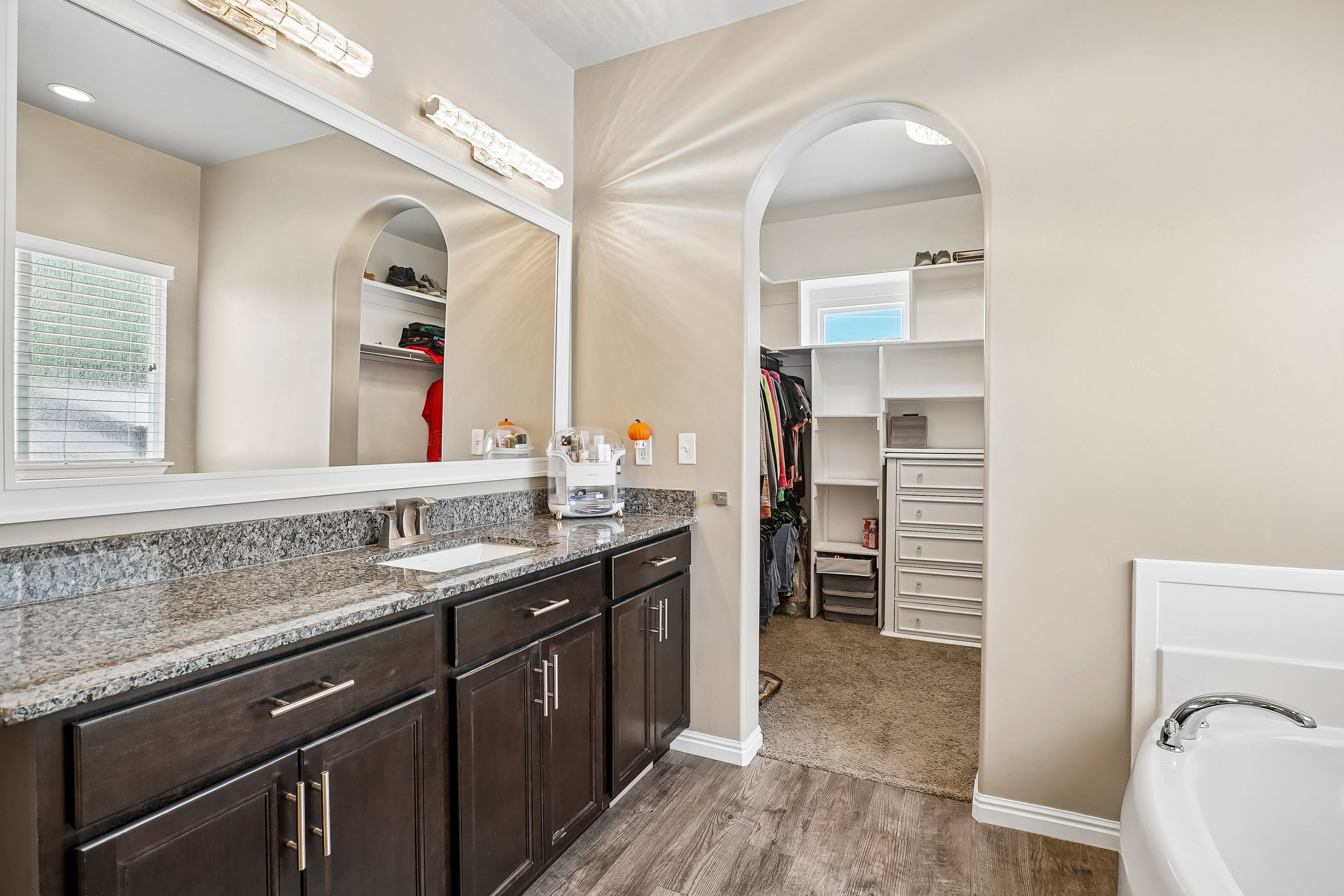 Bathroom vanity featuring a single undermount sink set in a gray granite countertop, dark wood-finish cabinetry with brushed nickel hardware, and an expansive wall-mounted mirror