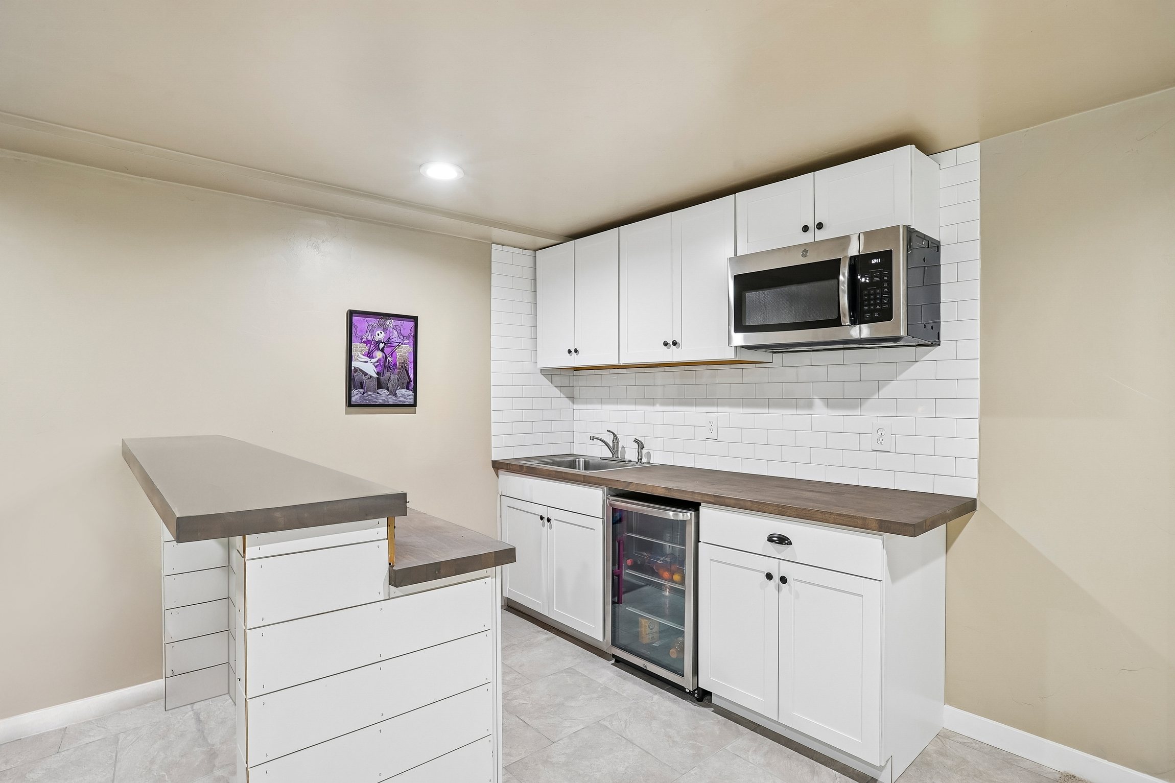 Compact kitchen area featuring white shaker cabinetry, subway tile backsplash, wood-finish countertops, and stainless steel appliances including an over-the-range microwave and beverage cooler