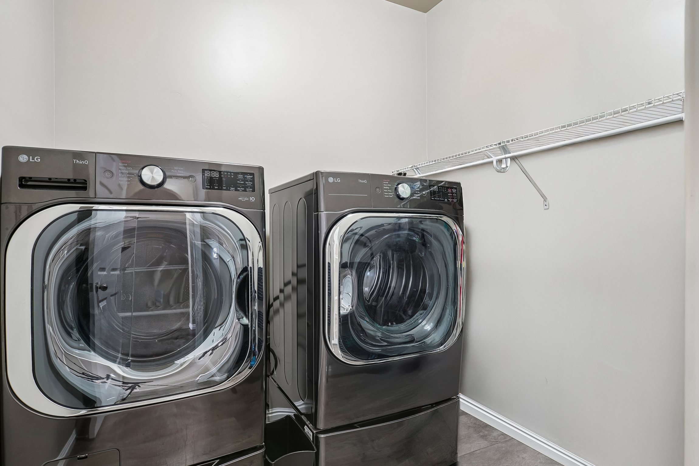 Laundry area featuring a front-loading washer and dryer set, neutral wall paint, and a wire storage shelf