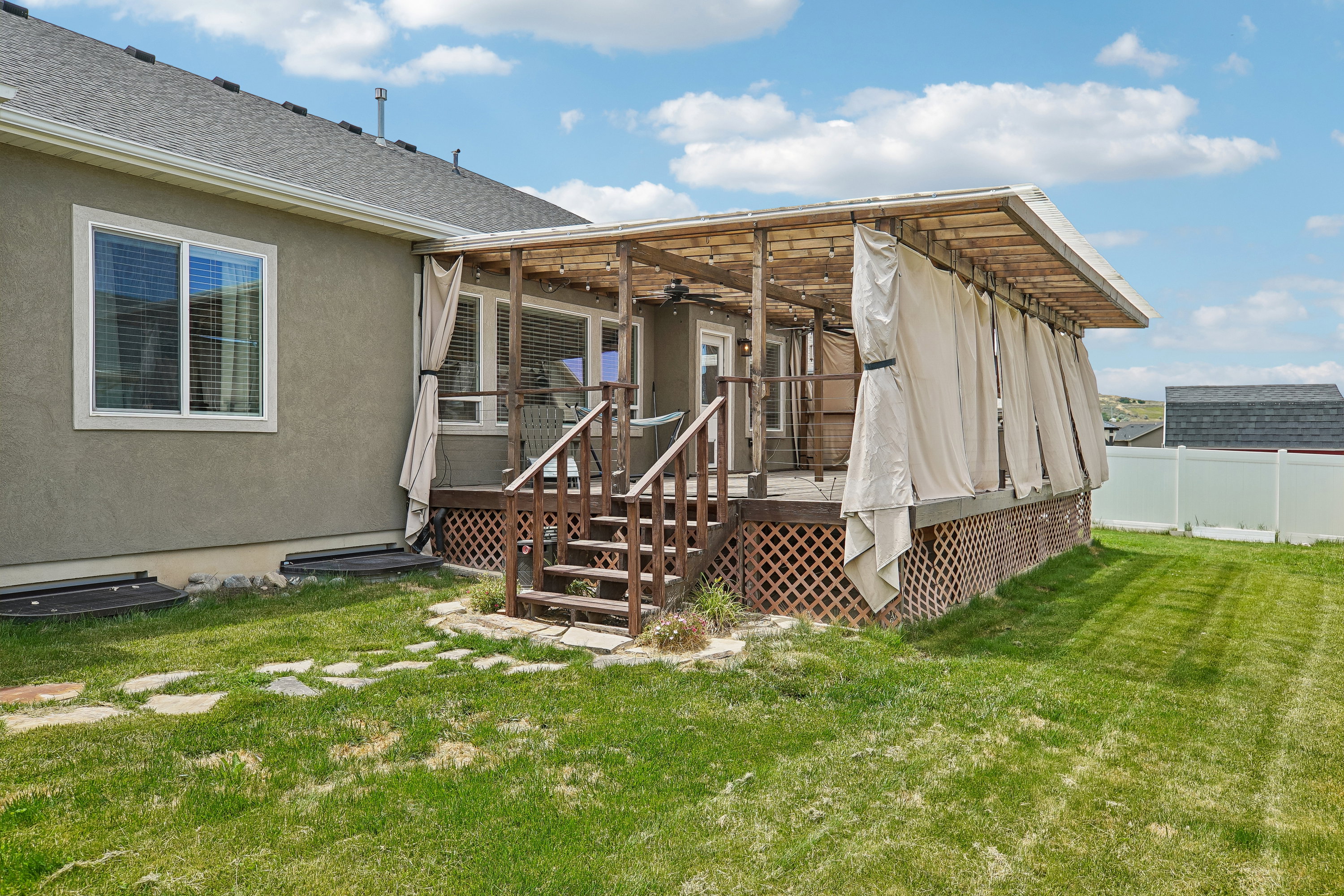 Expansive rear deck featuring a wooden pergola, privacy drapes, and lattice skirting