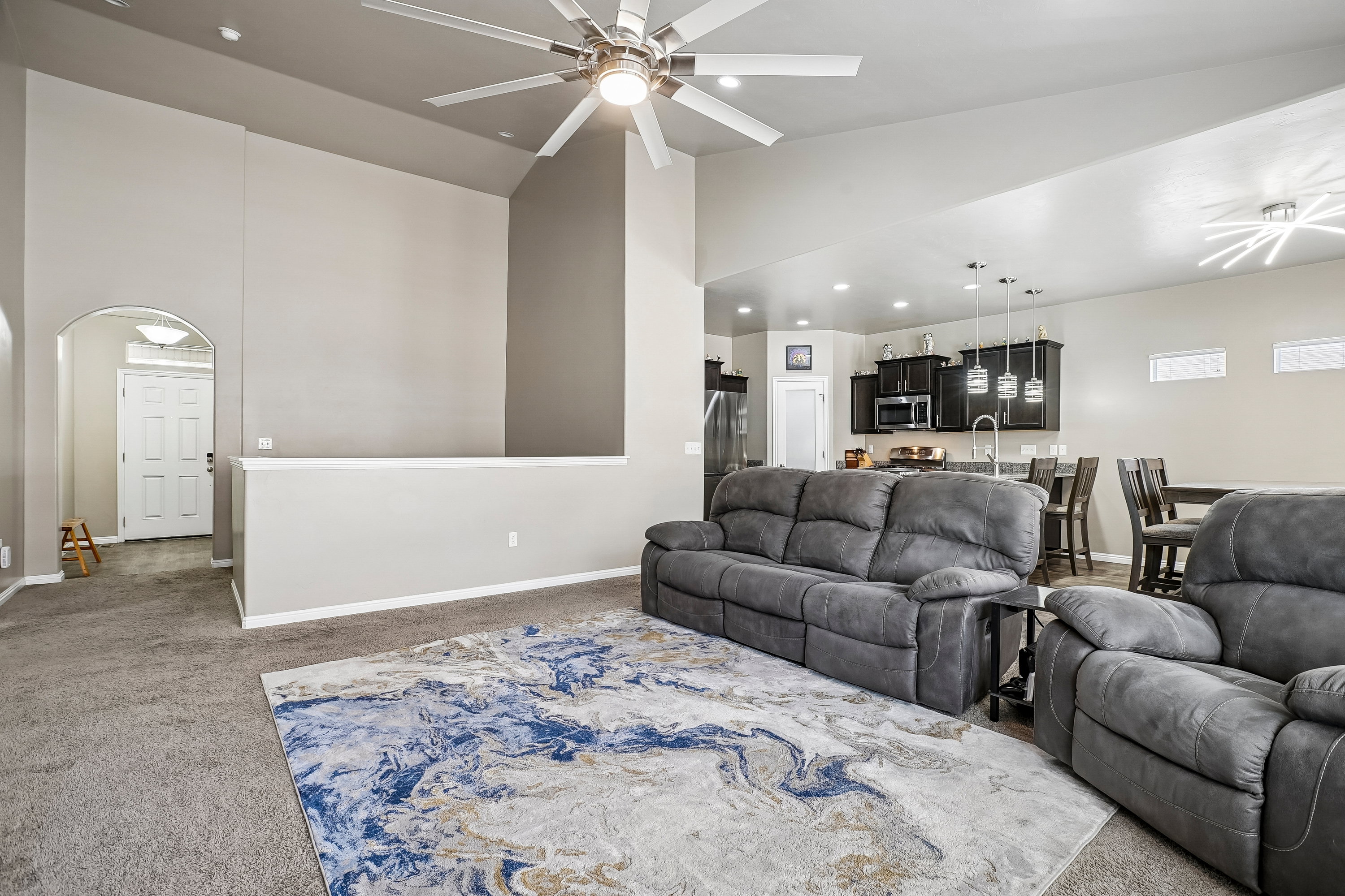 Open-concept living area featuring vaulted ceilings, a ceiling fan with integrated lighting, and a partial wall separating spaces