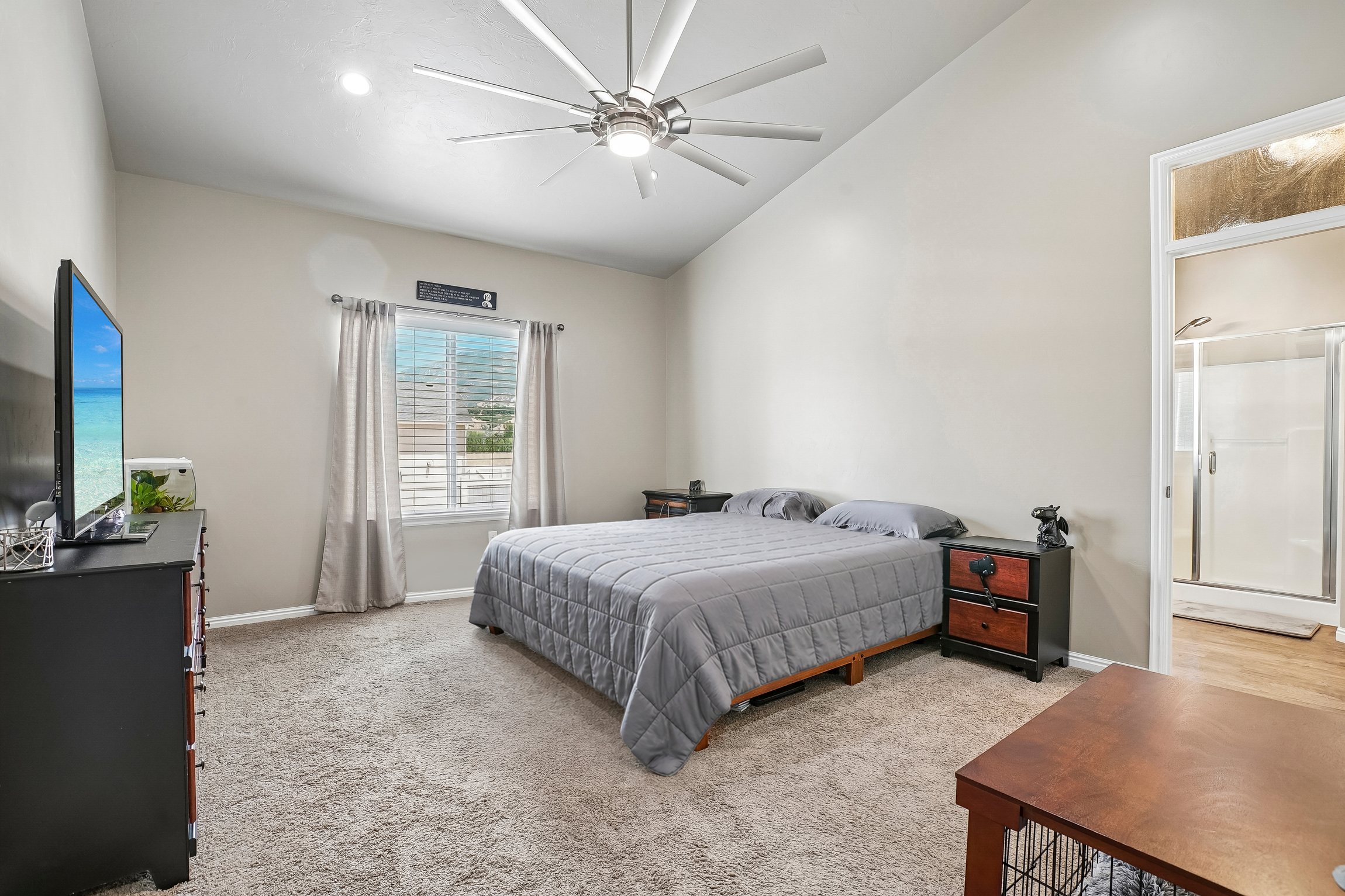 Spacious room featuring vaulted ceilings, a large window, neutral carpeting, and a ceiling fan with integrated lighting