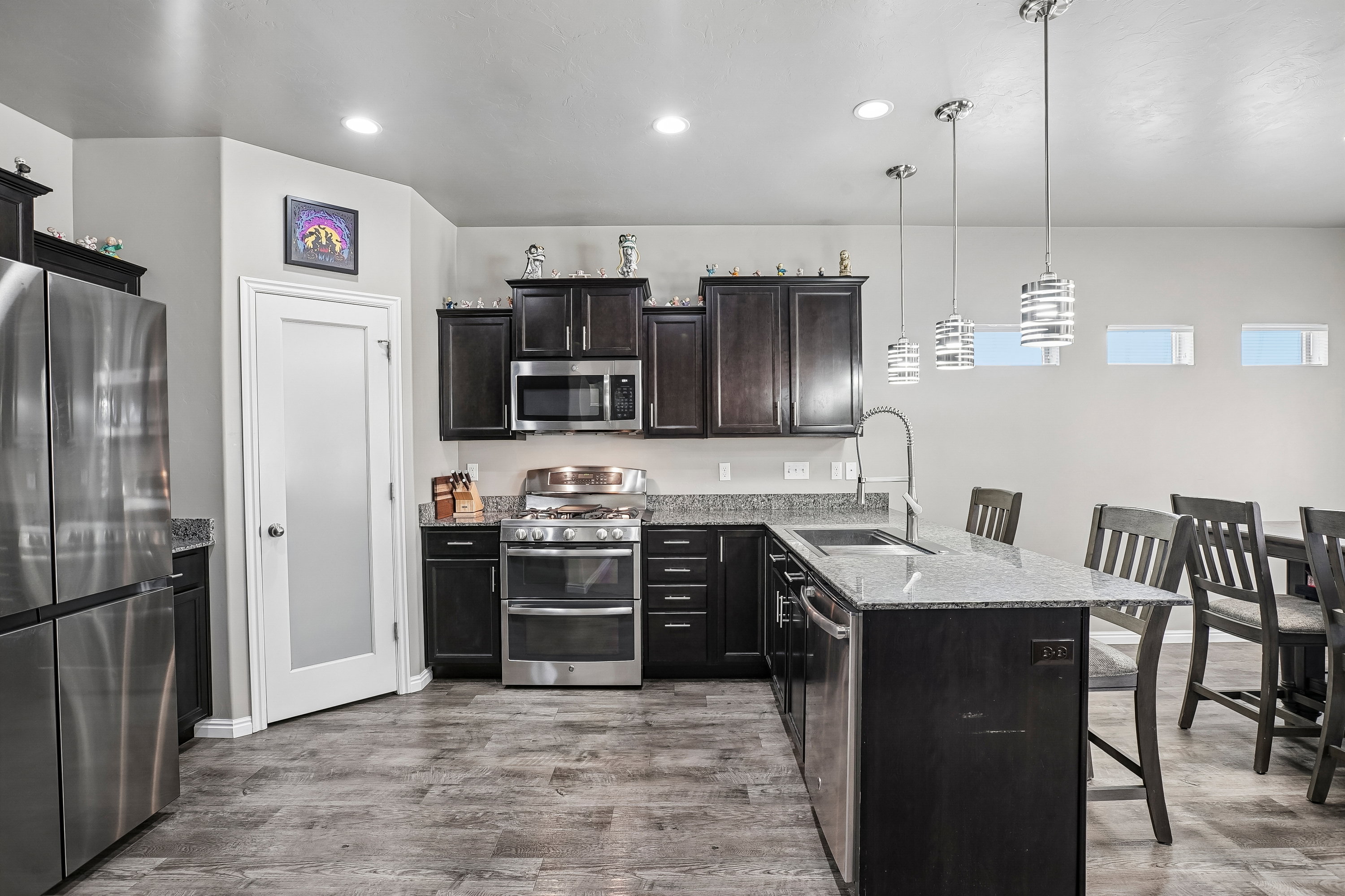 Kitchen featuring wood-finish flooring, dark wood cabinetry, stainless steel appliances, and a central island with a sink and granite-style countertop