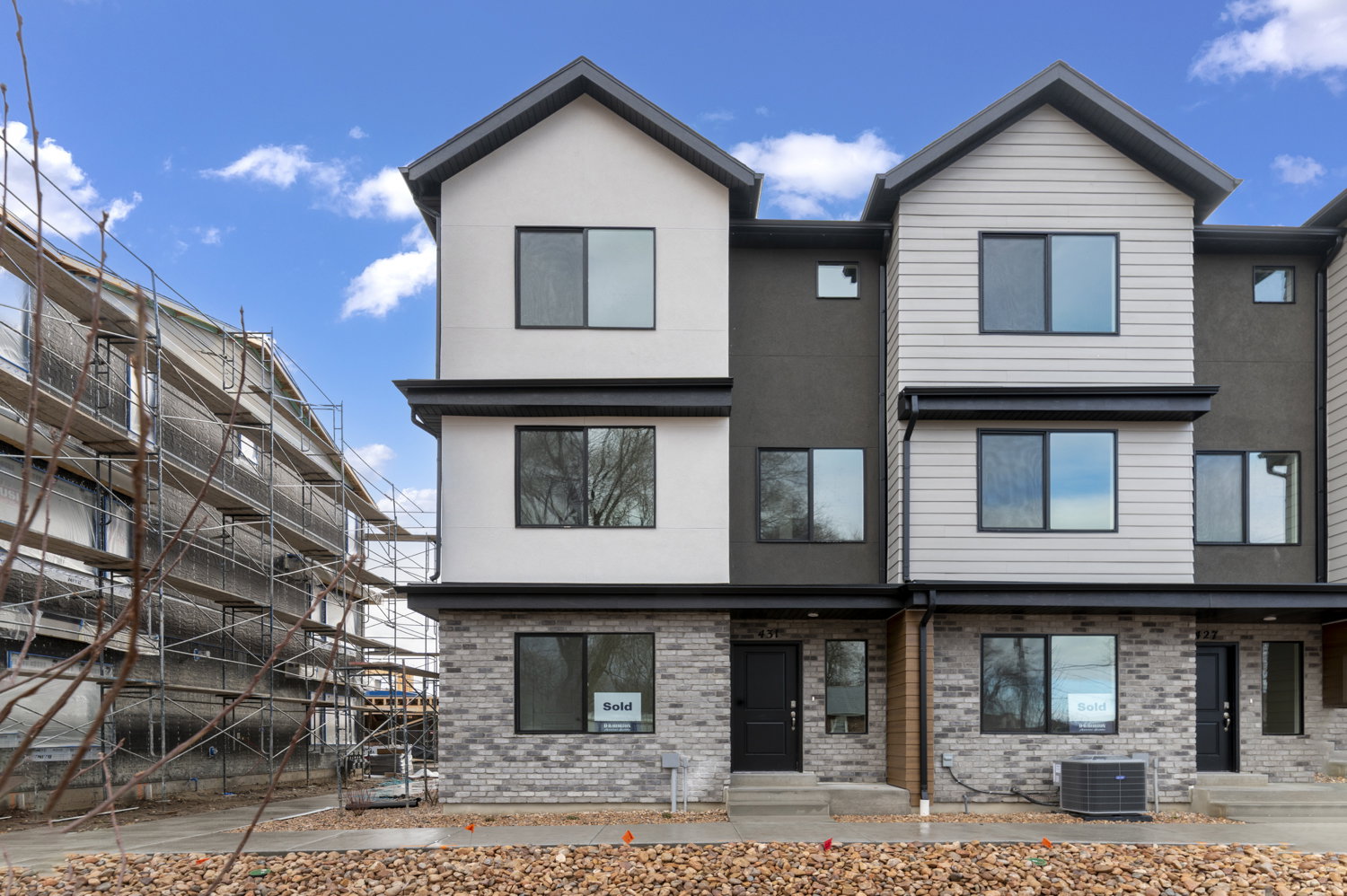 Multi-story townhome with a modern facade featuring contrasting light and dark siding, brick veneer accents, and black-framed windows