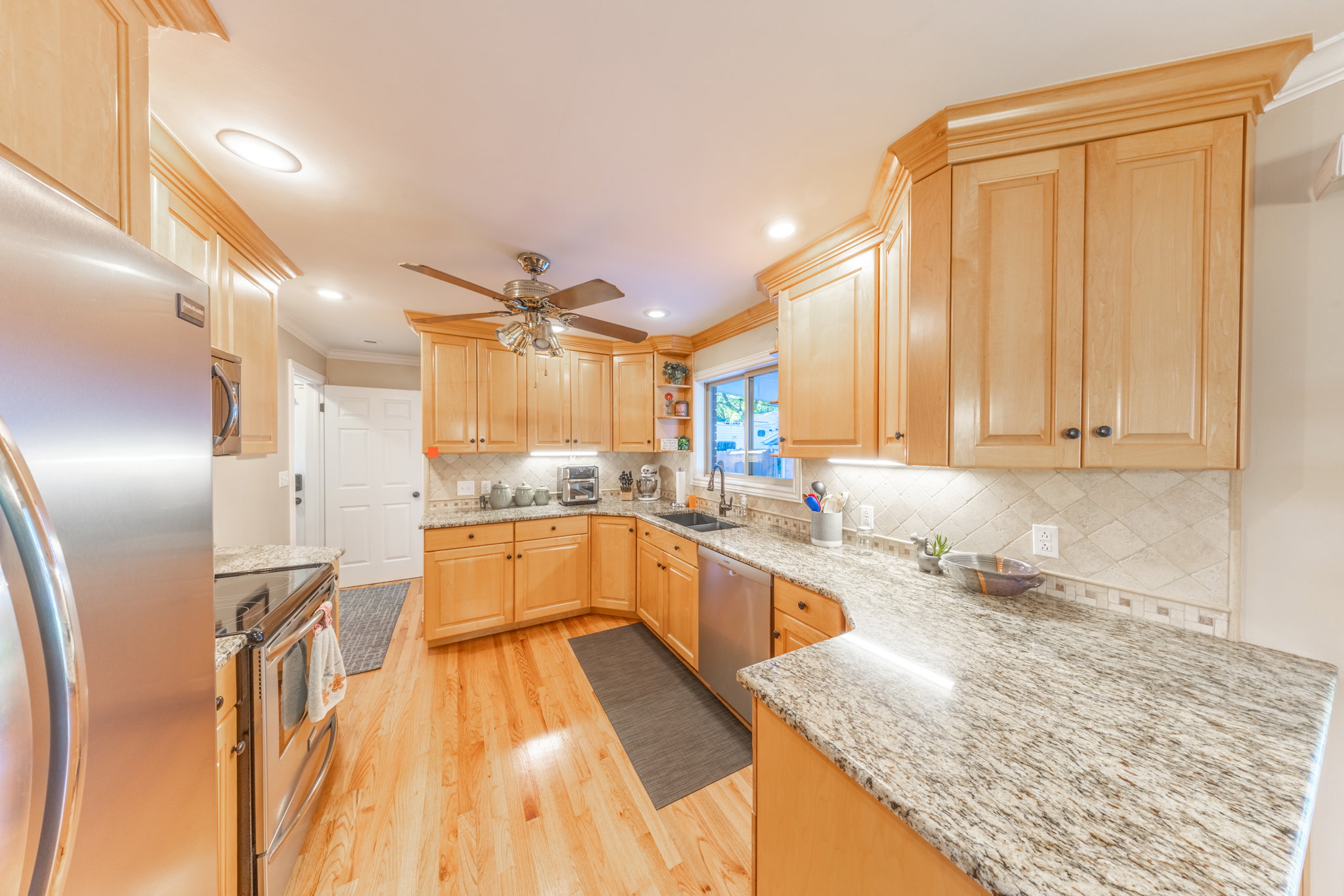 Kitchen featuring wood-finish flooring, light wood cabinetry, stone countertops, a tile backsplash, and stainless steel appliances