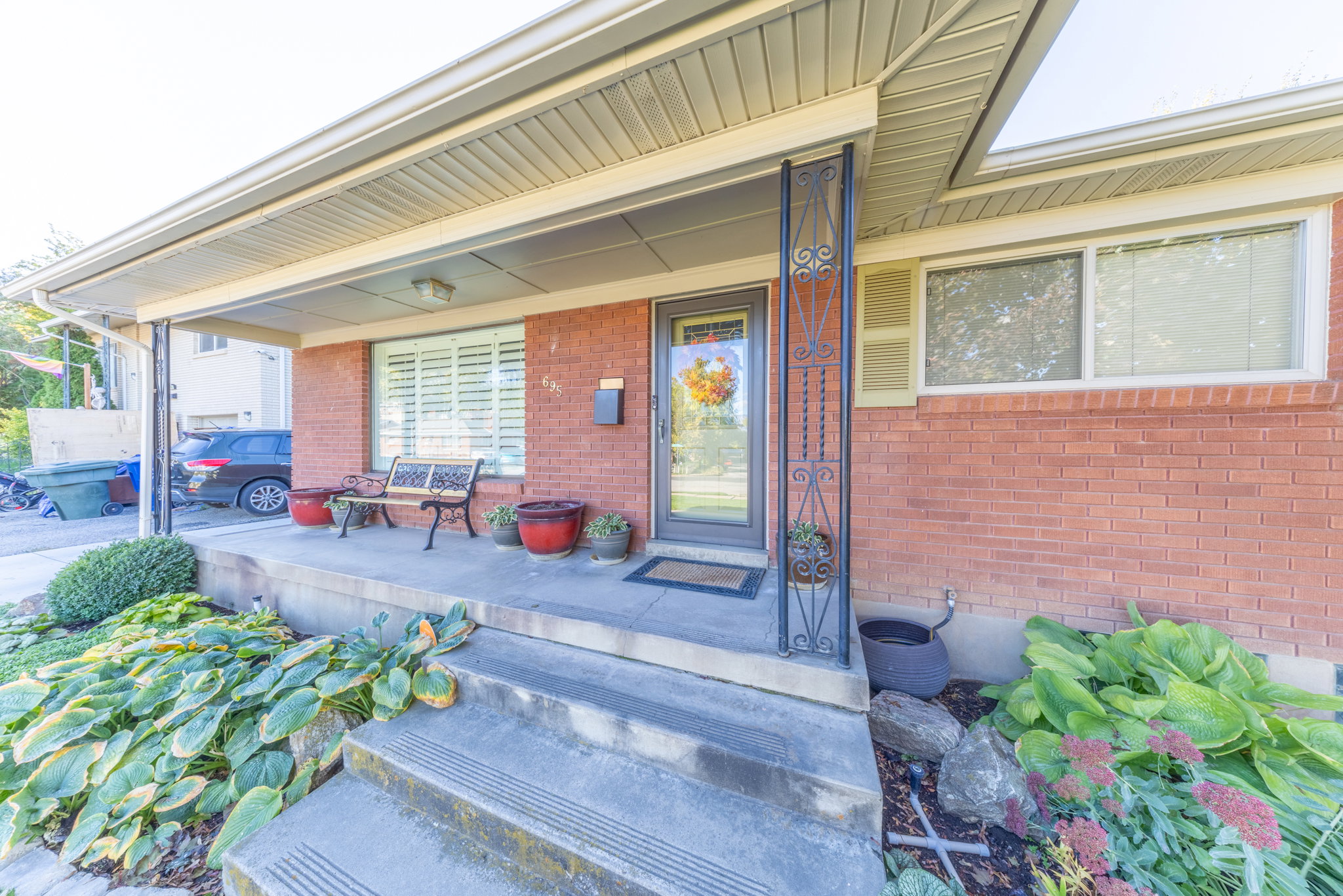Brick exterior featuring a covered porch with concrete steps, wrought iron column, and a glass-paneled entry door