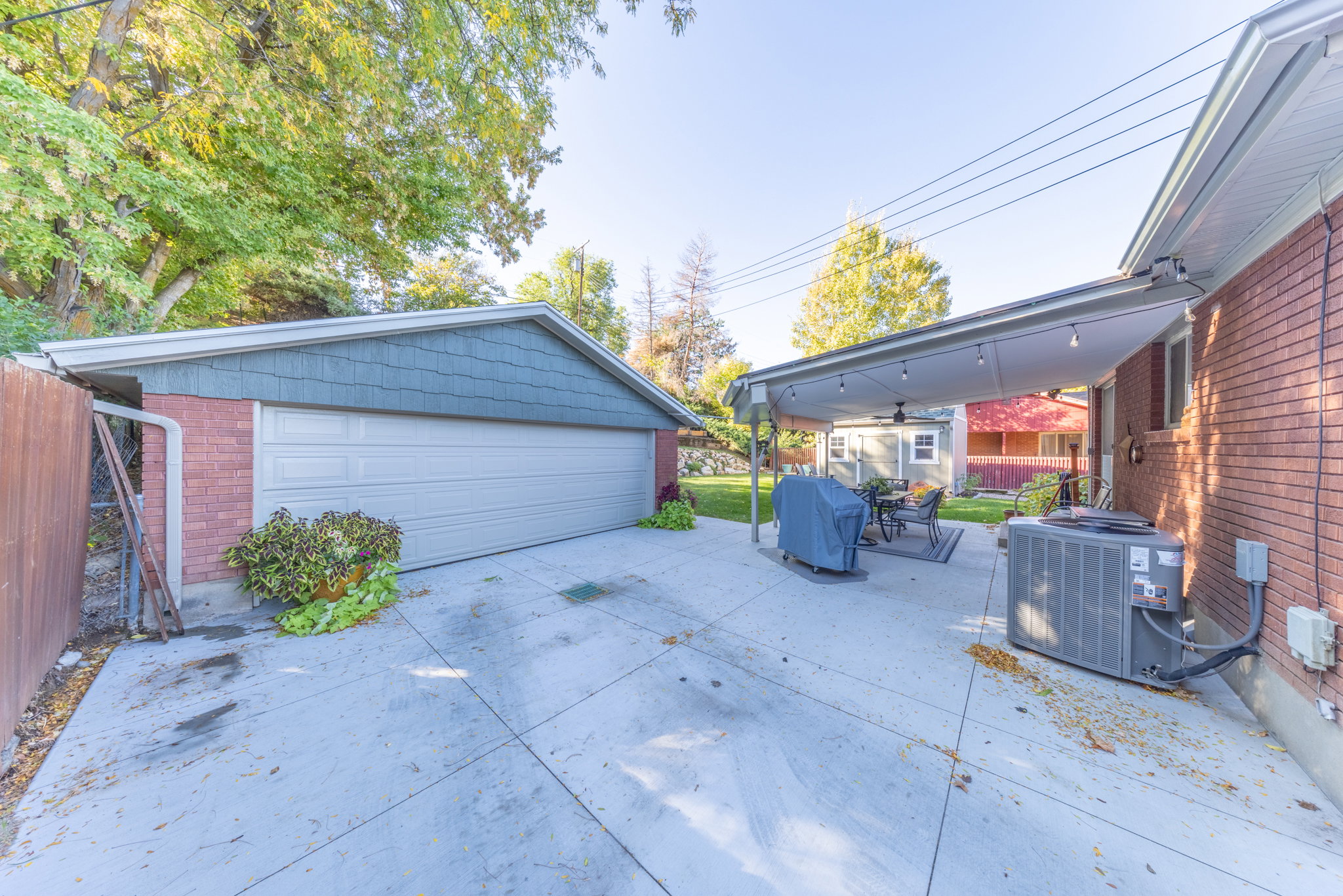 Spacious concrete driveway featuring a detached garage with a light gray door and an attached covered patio with string lighting and a ceiling fan