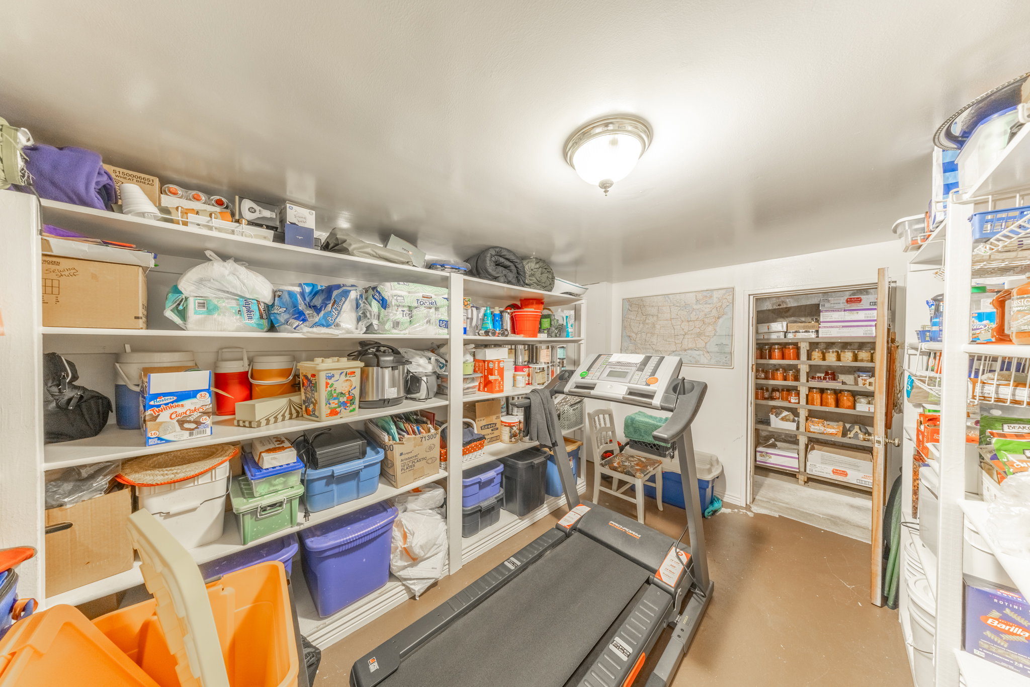 Spacious storage room featuring extensive built-in shelving, a neutral color palette, ceiling-mounted lighting, and an additional storage closet