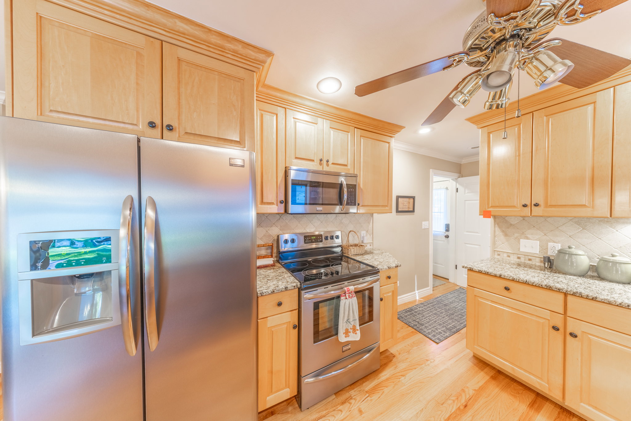 Kitchen featuring light wood cabinetry with crown molding, stainless steel appliances, granite countertops, and wood-finish flooring