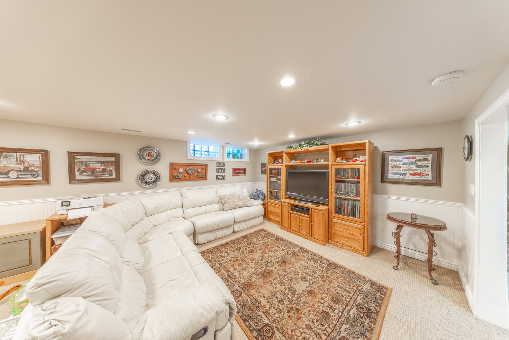 Recessed lighting illuminates this versatile room, featuring a built-in wood-finish media console, light-toned carpeting, and wainscoting