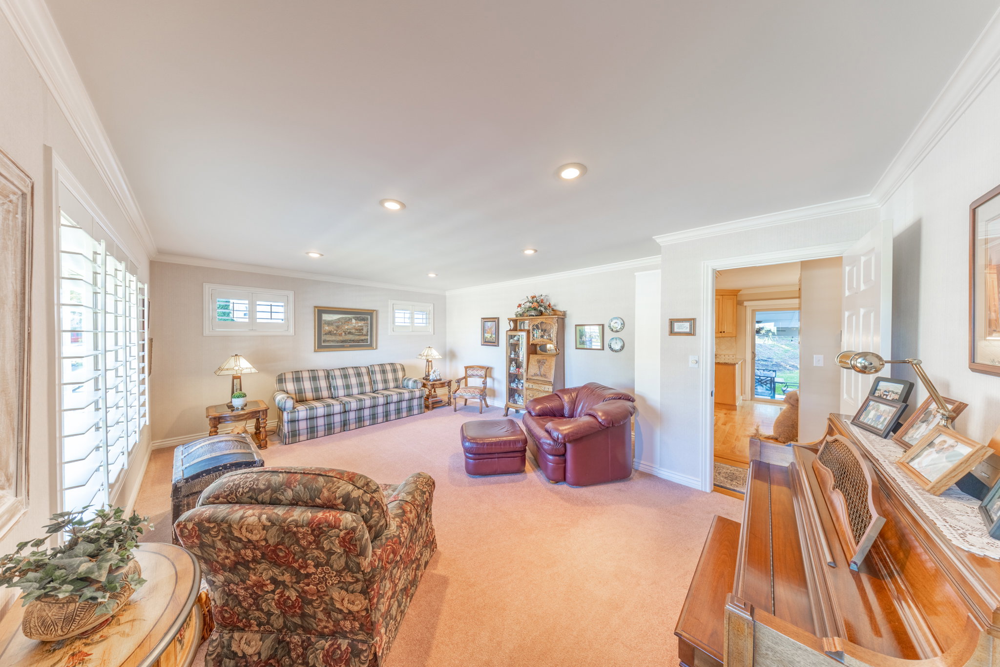 Spacious living area featuring neutral wall tones, recessed lighting, crown molding, and plantation shutters