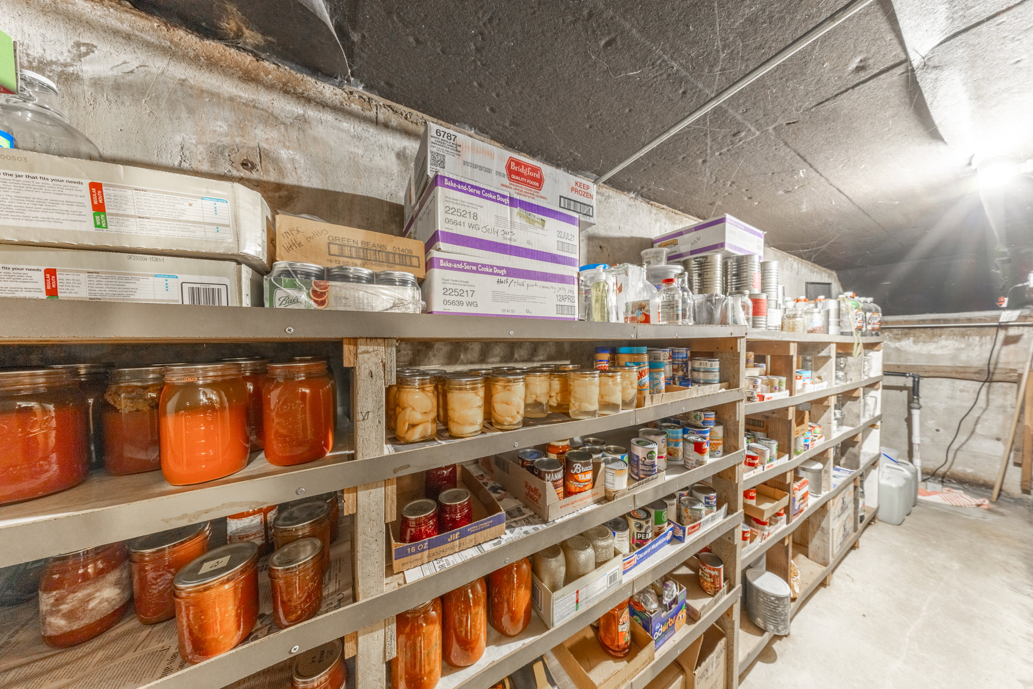 Extensive unfinished storage room featuring exposed concrete walls and ceiling, full-height shelving units, and a concrete floor
