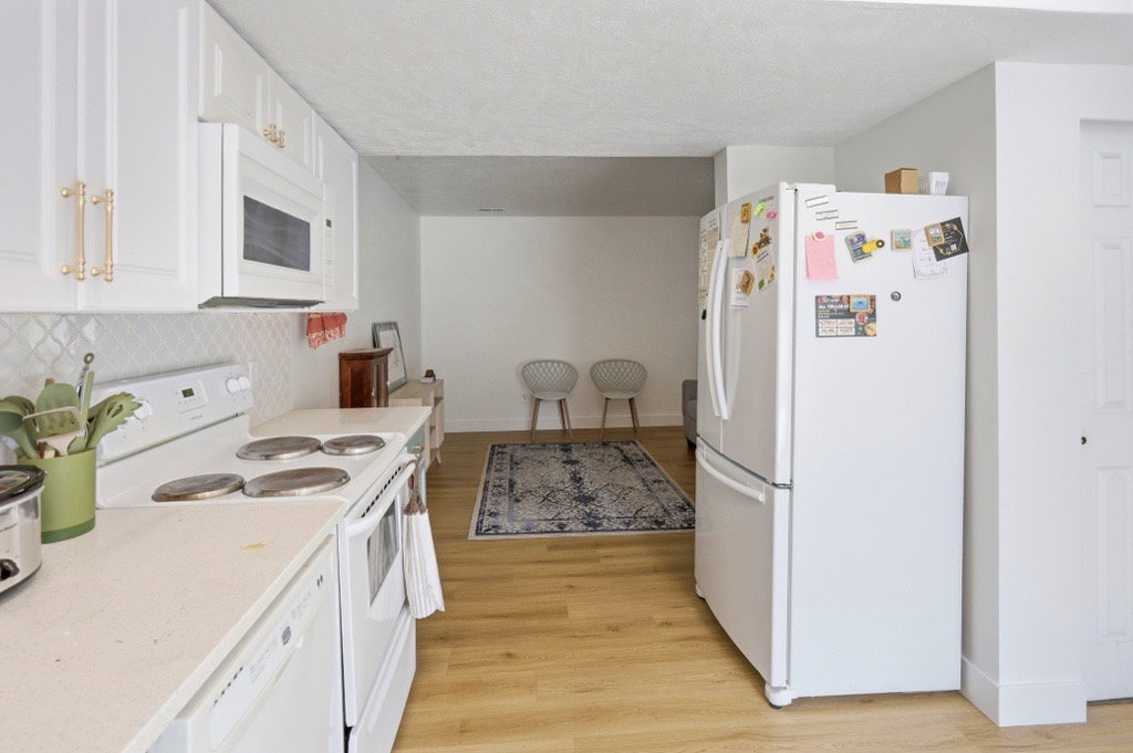 Kitchen featuring white cabinetry with gold-tone hardware, white appliances, and a white patterned tile backsplash