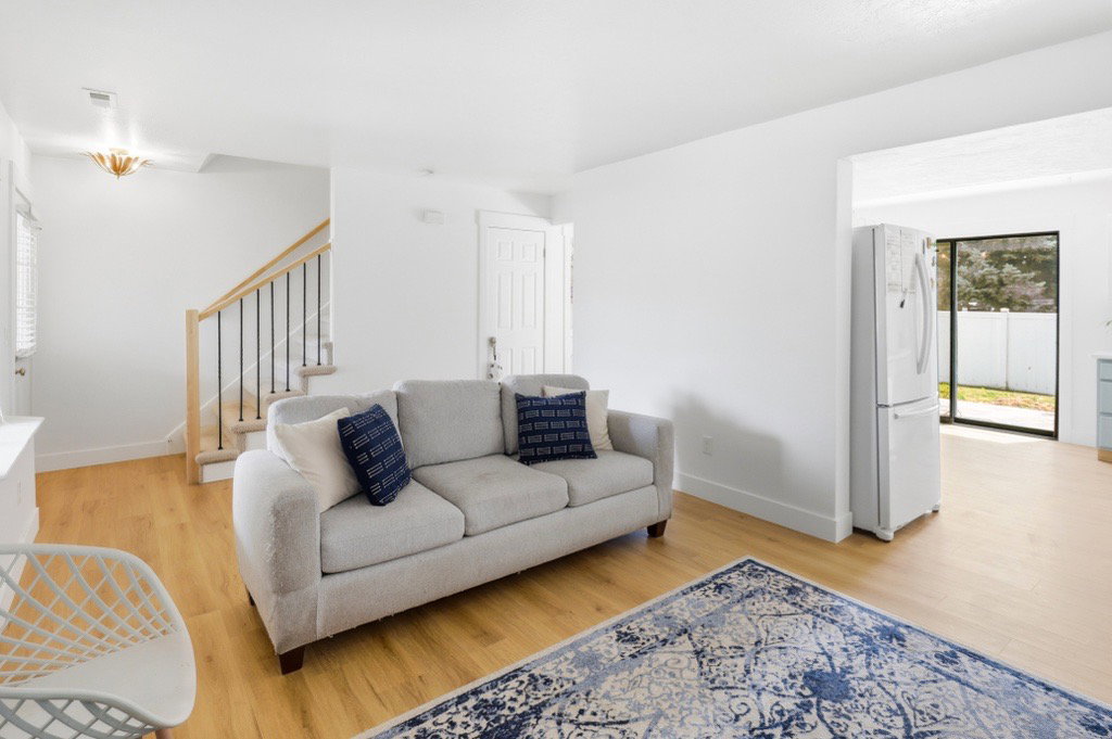 Open-concept living space featuring wood-finish flooring, white walls, and a staircase with natural wood railings and black balusters
