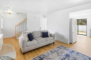 Open-concept living space featuring wood-finish flooring, white walls, and a staircase with natural wood railings and black balusters