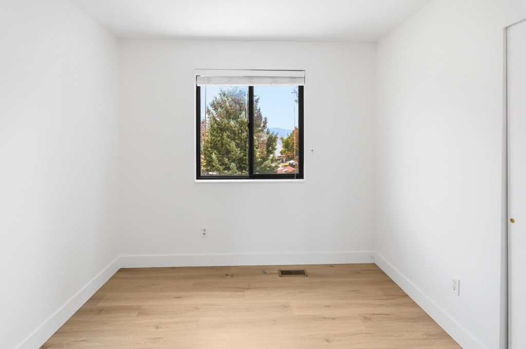 Bright room featuring a large window with black framing, wood-finish flooring, white walls, white baseboards, and a white closet door